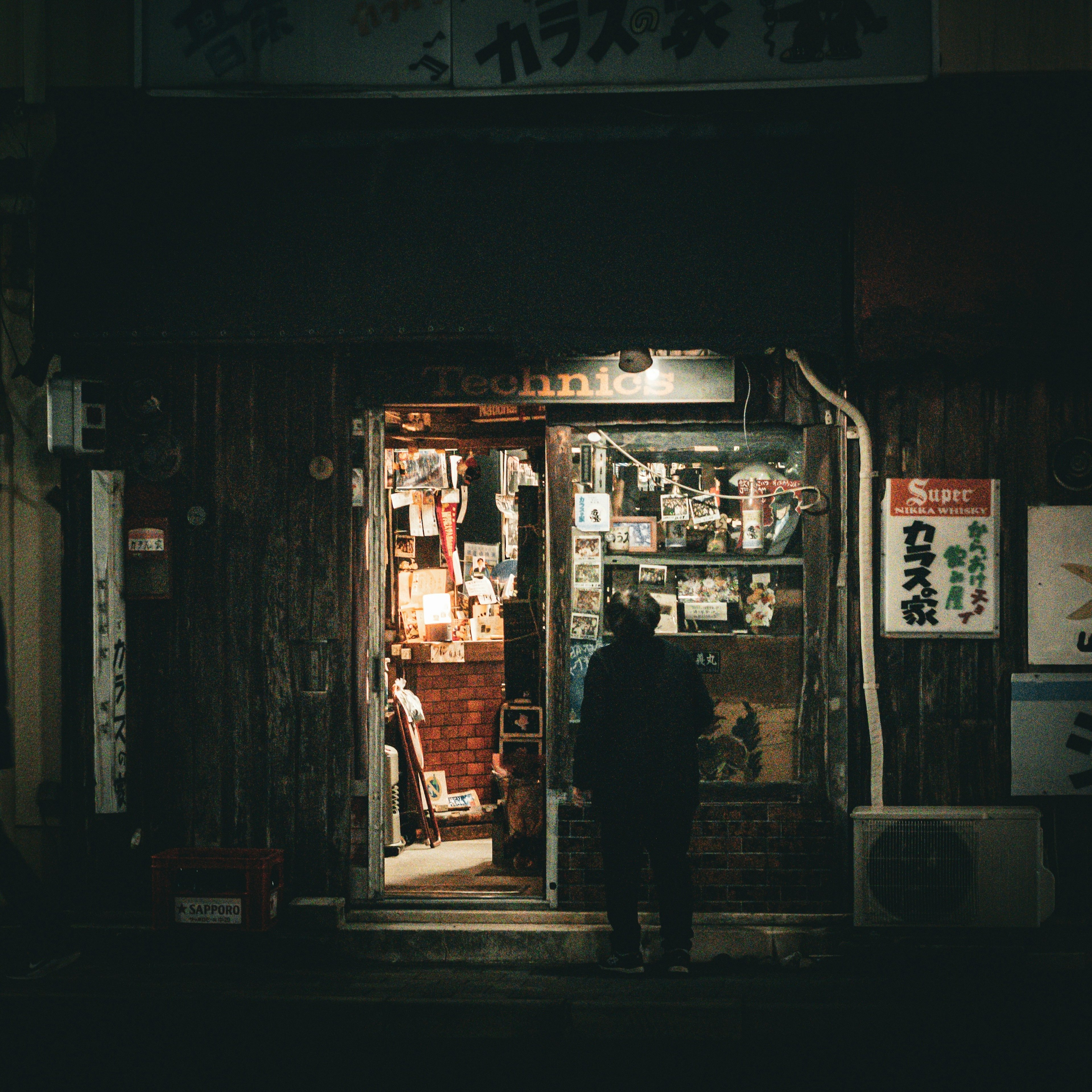 Exterior of a small bookstore illuminated at night with a person standing outside