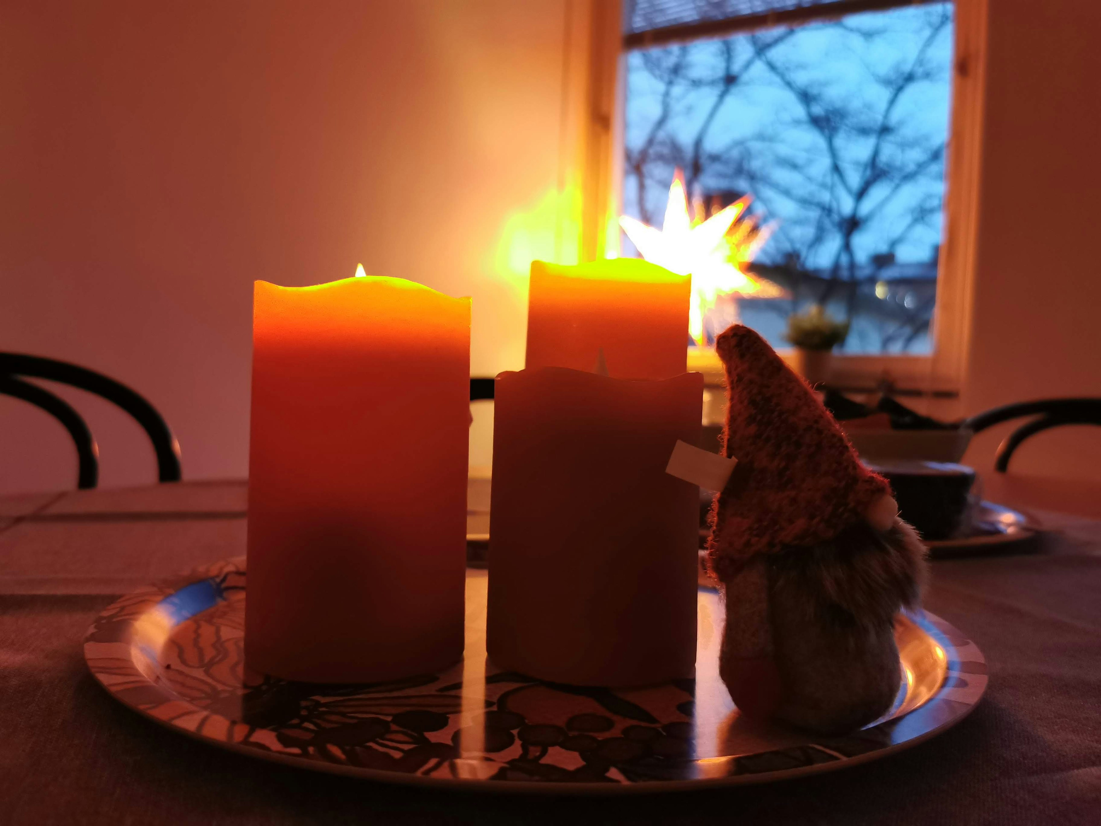 Two lit orange candles on a silver tray with a small figure in a cozy room at dusk