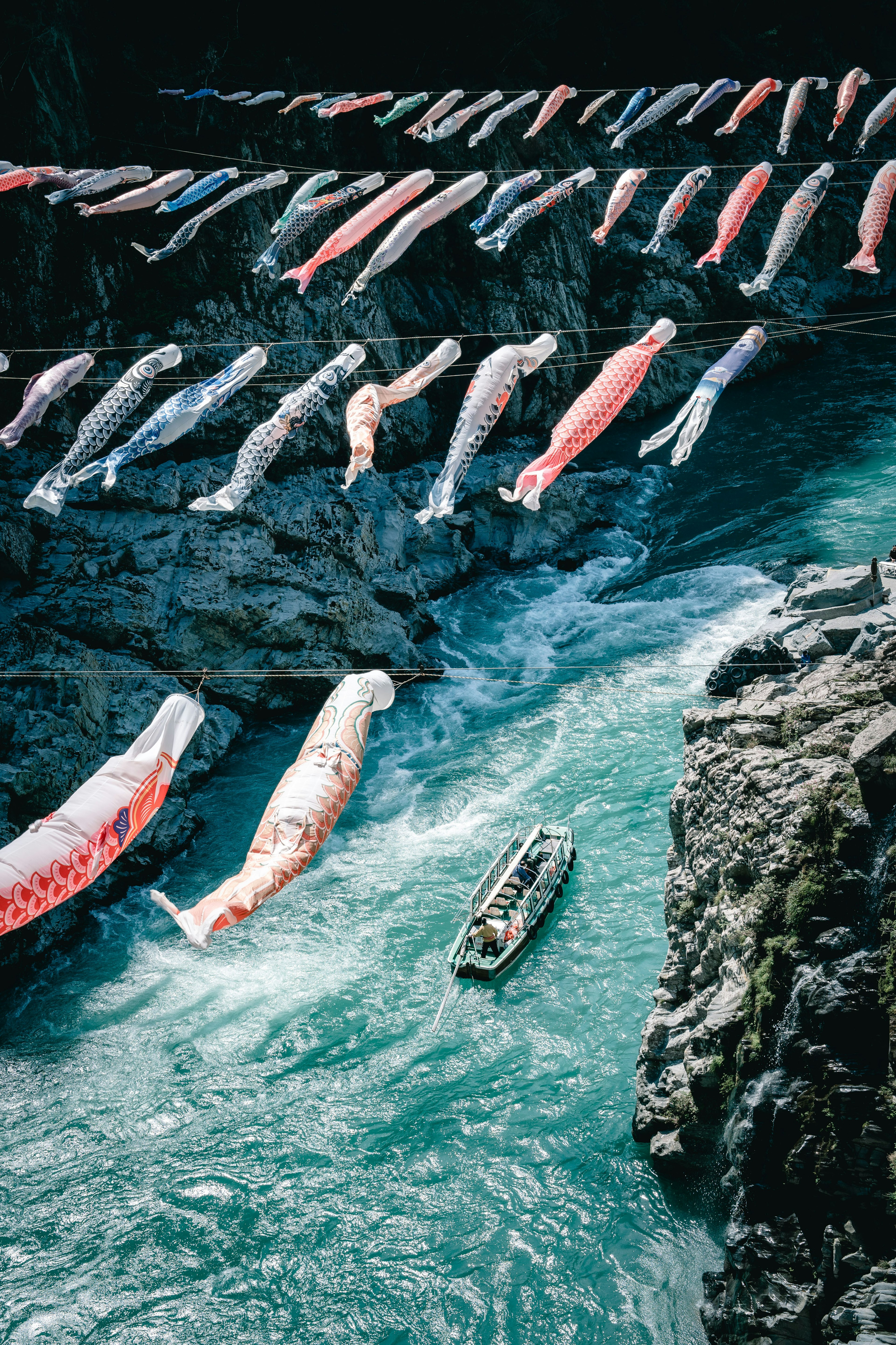 Bunte Koinobori-Flaggen, die über einem Fluss hängen, mit einem kleinen Boot, das schwimmt