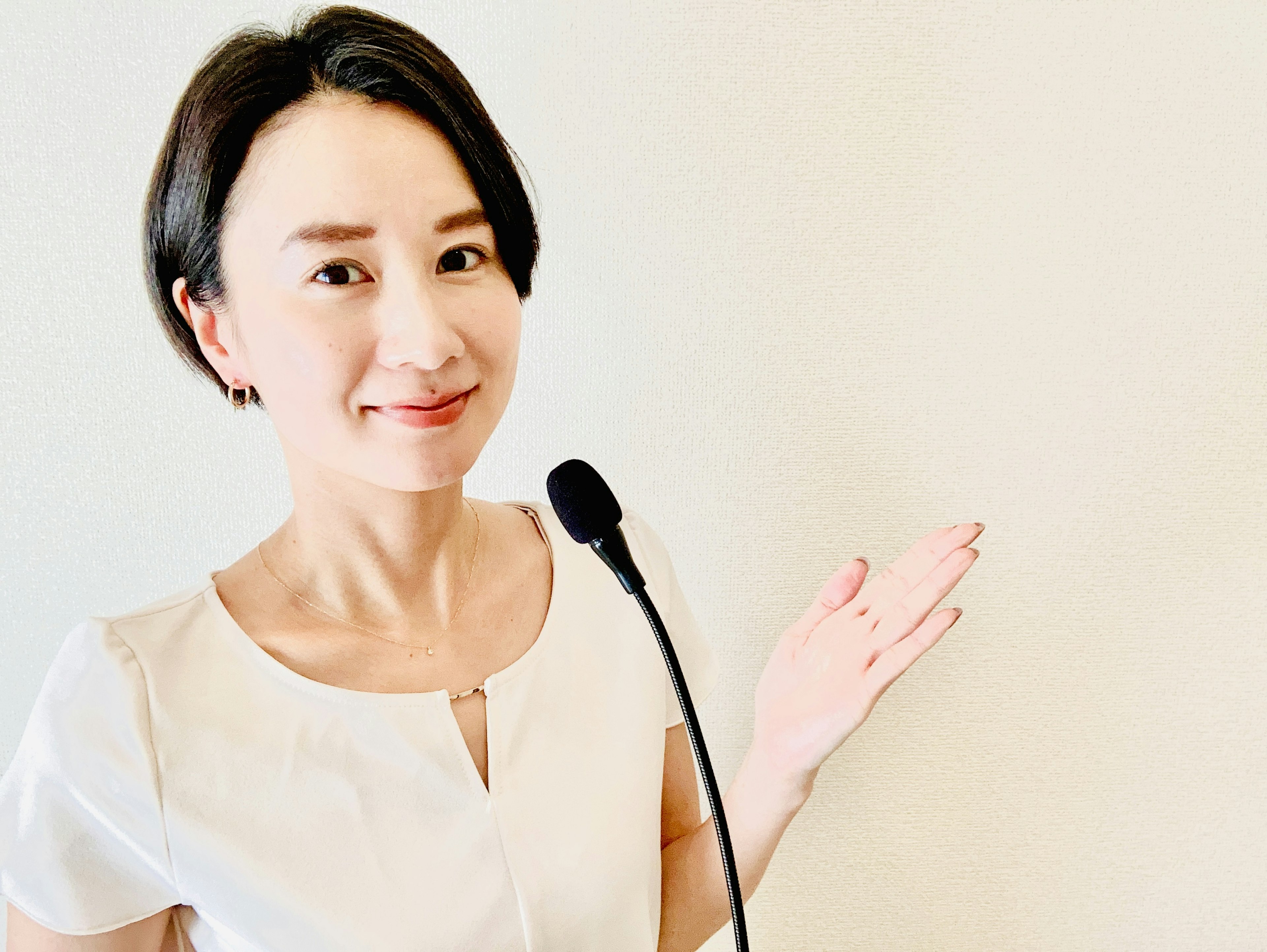 A woman in a white top gestures towards the side while speaking into a microphone