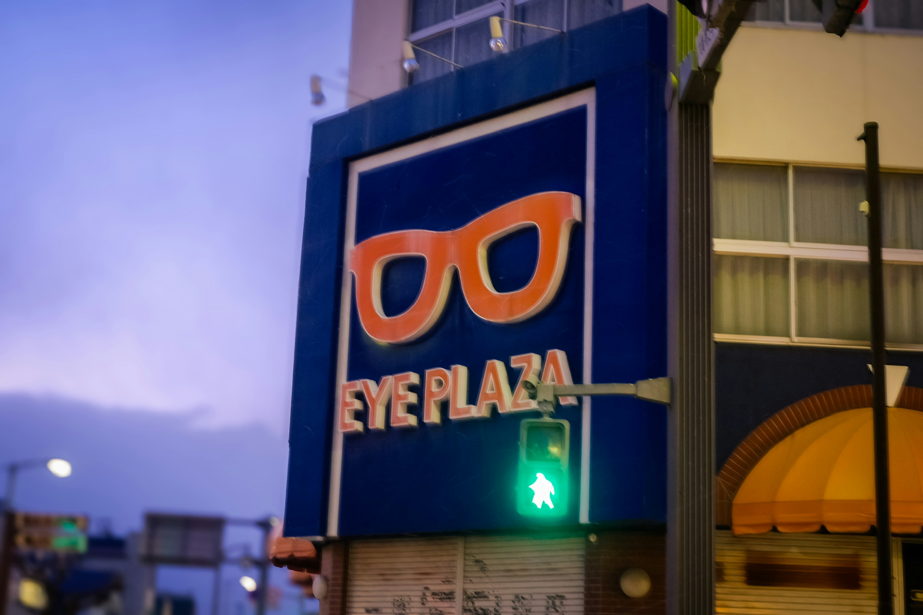 Schild von Eye Plaza mit orangefarbenem Brillenlogo auf blauem Hintergrund