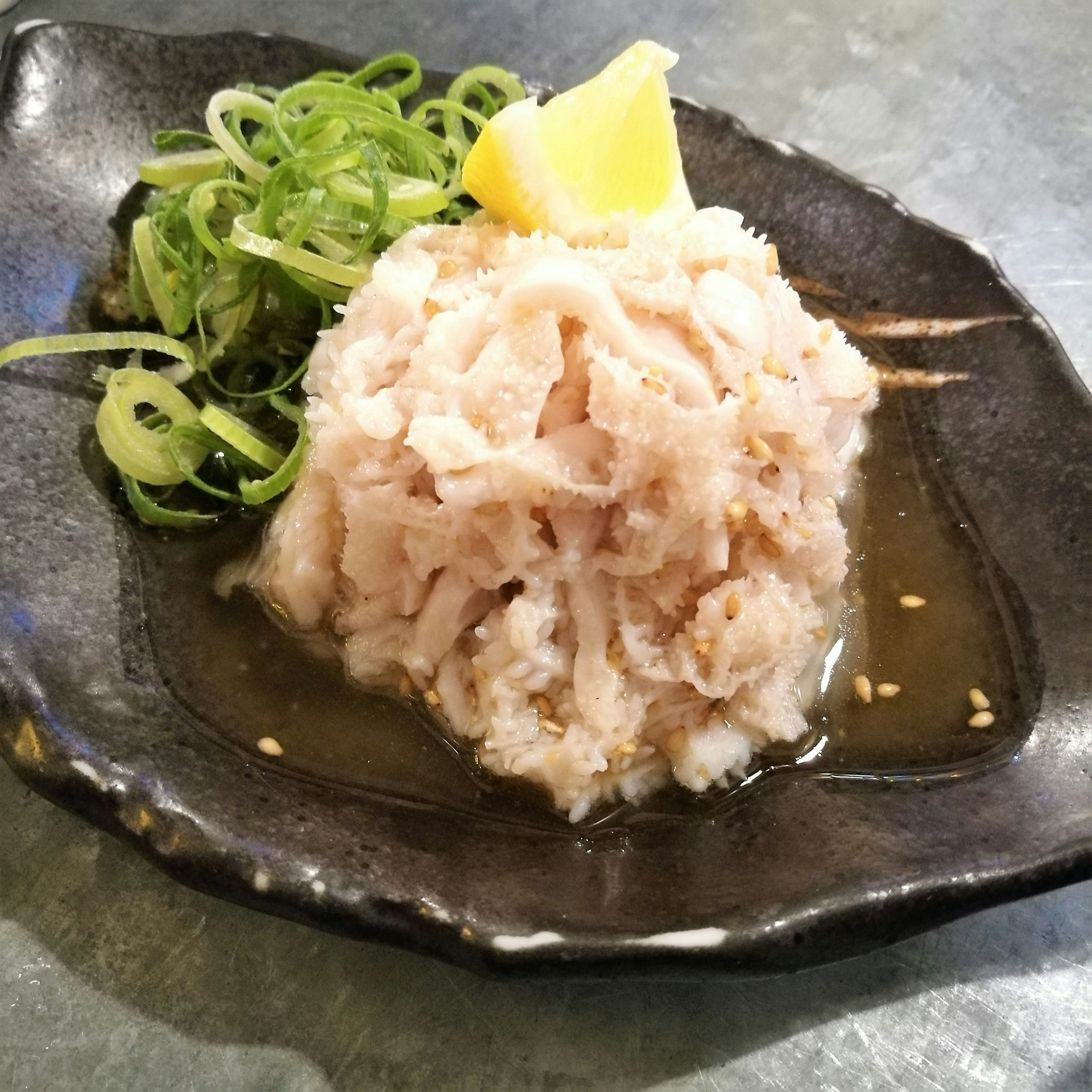 Sliced fish sashimi topped with green onions and lemon