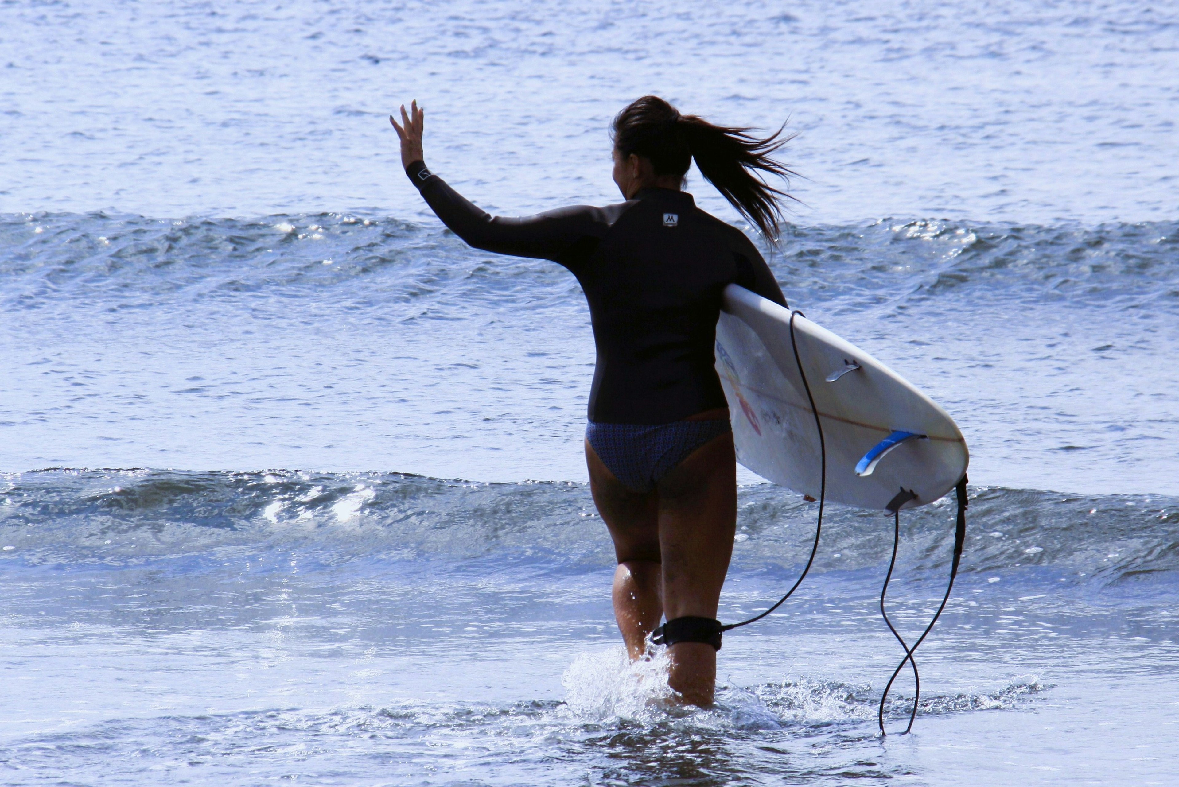 Woman walking towards the ocean holding a surfboard