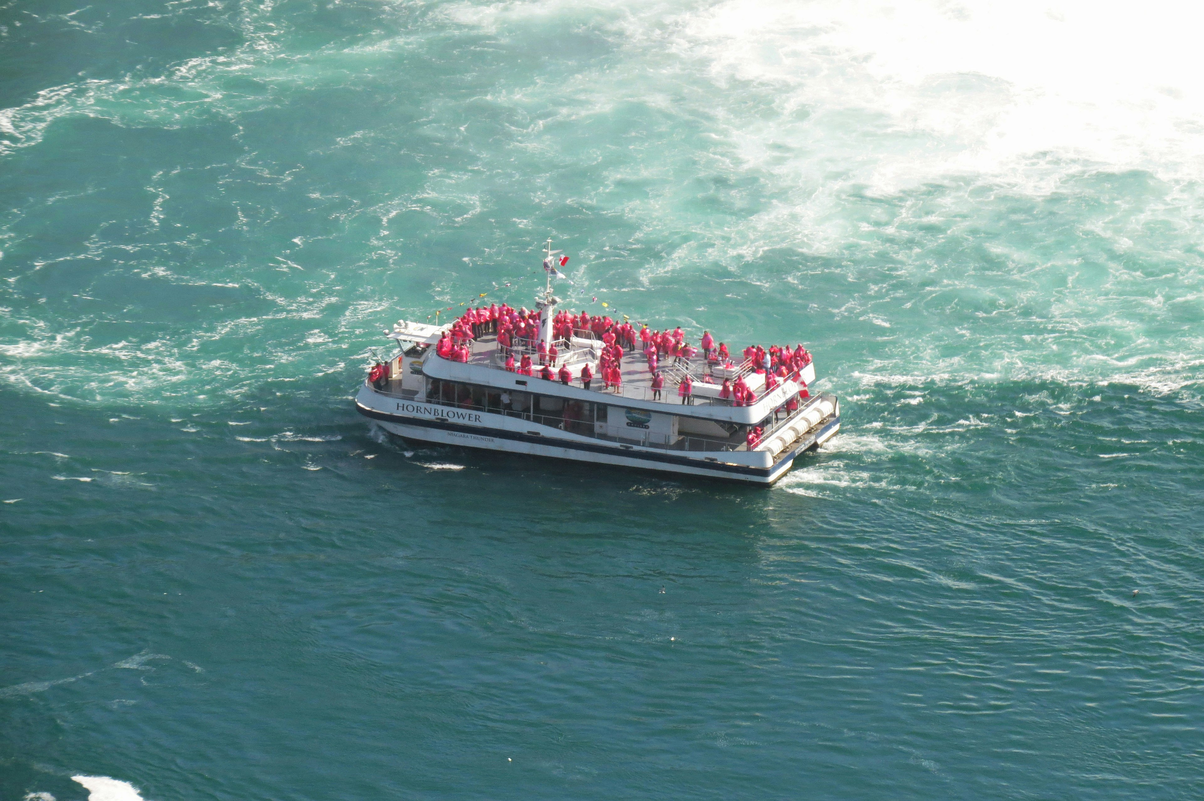 Barco turístico rodeado de agua con pasajeros vestidos de rojo