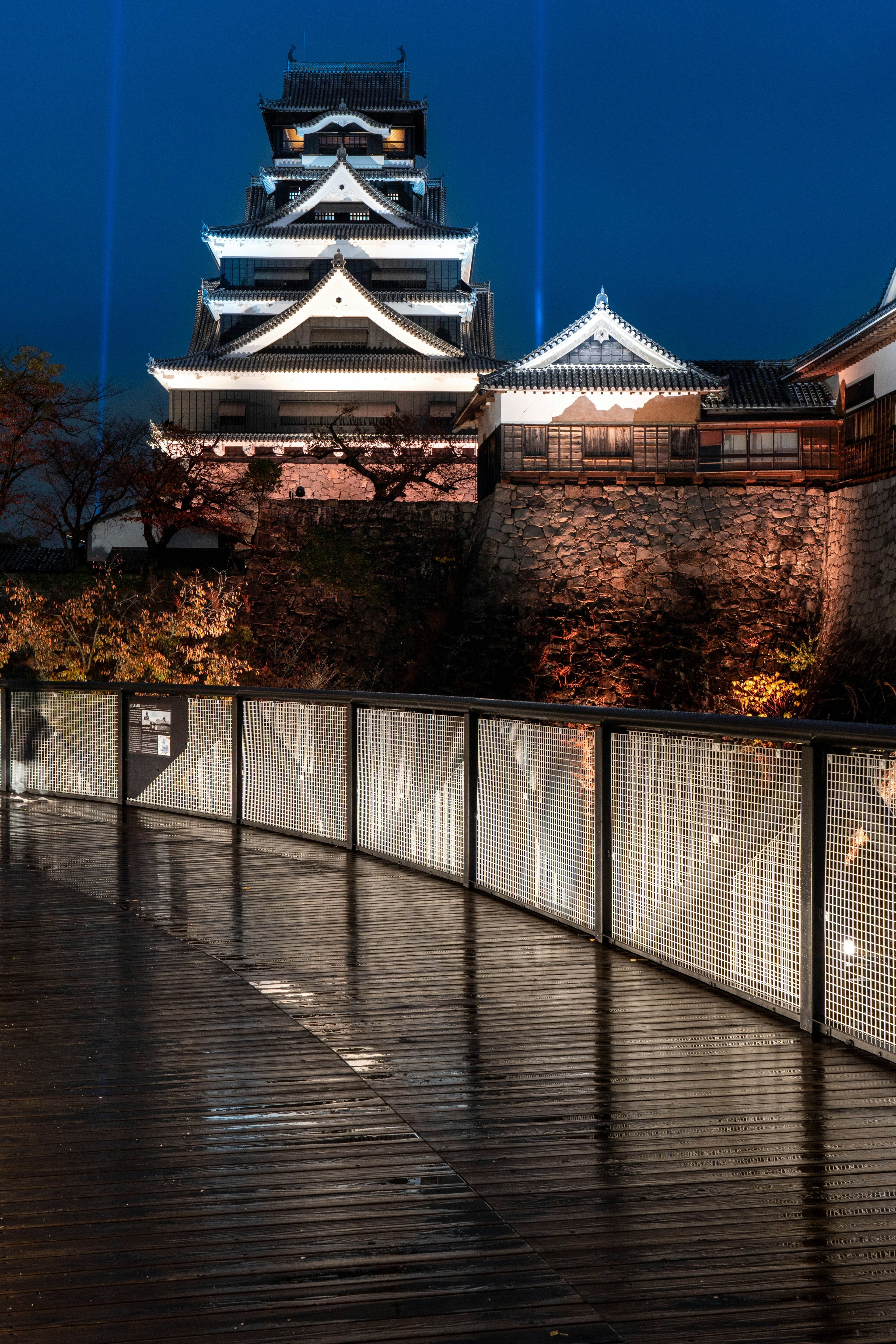 Illuminated castle at night with reflections on wooden walkway