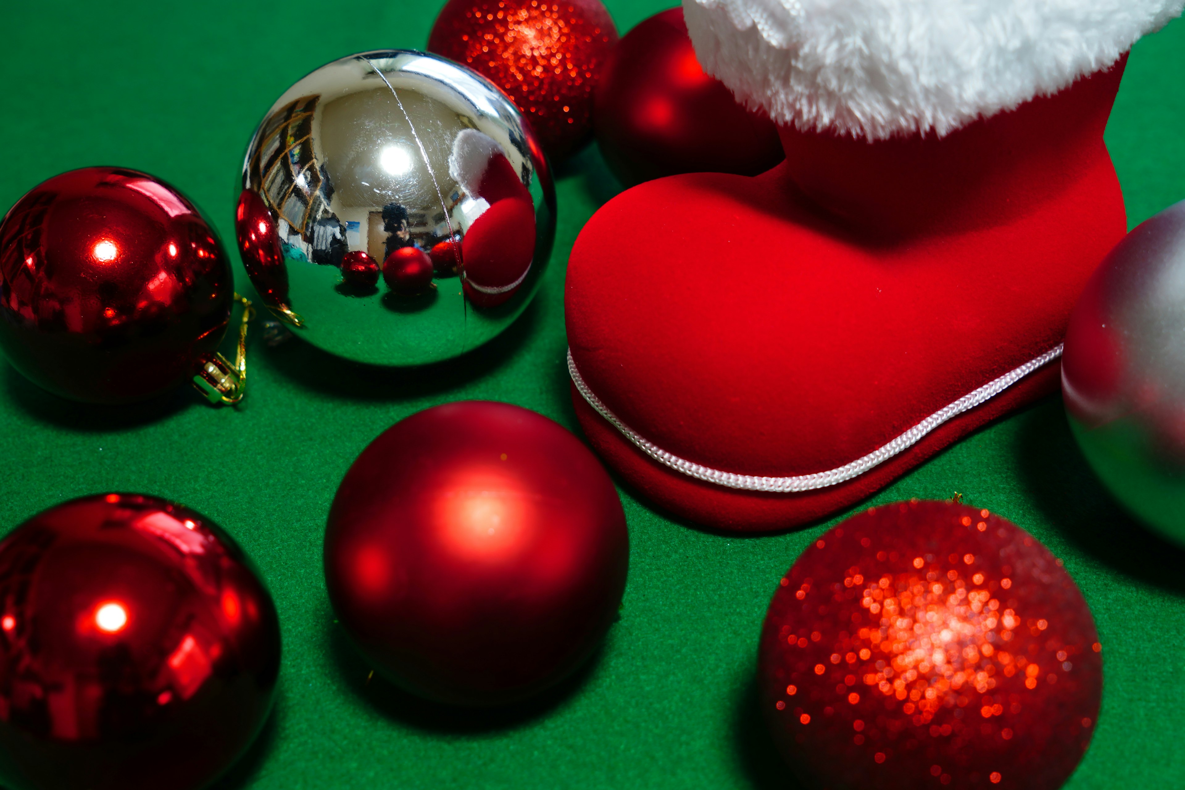 Red Santa boot with shiny red and silver Christmas ornaments on a green background