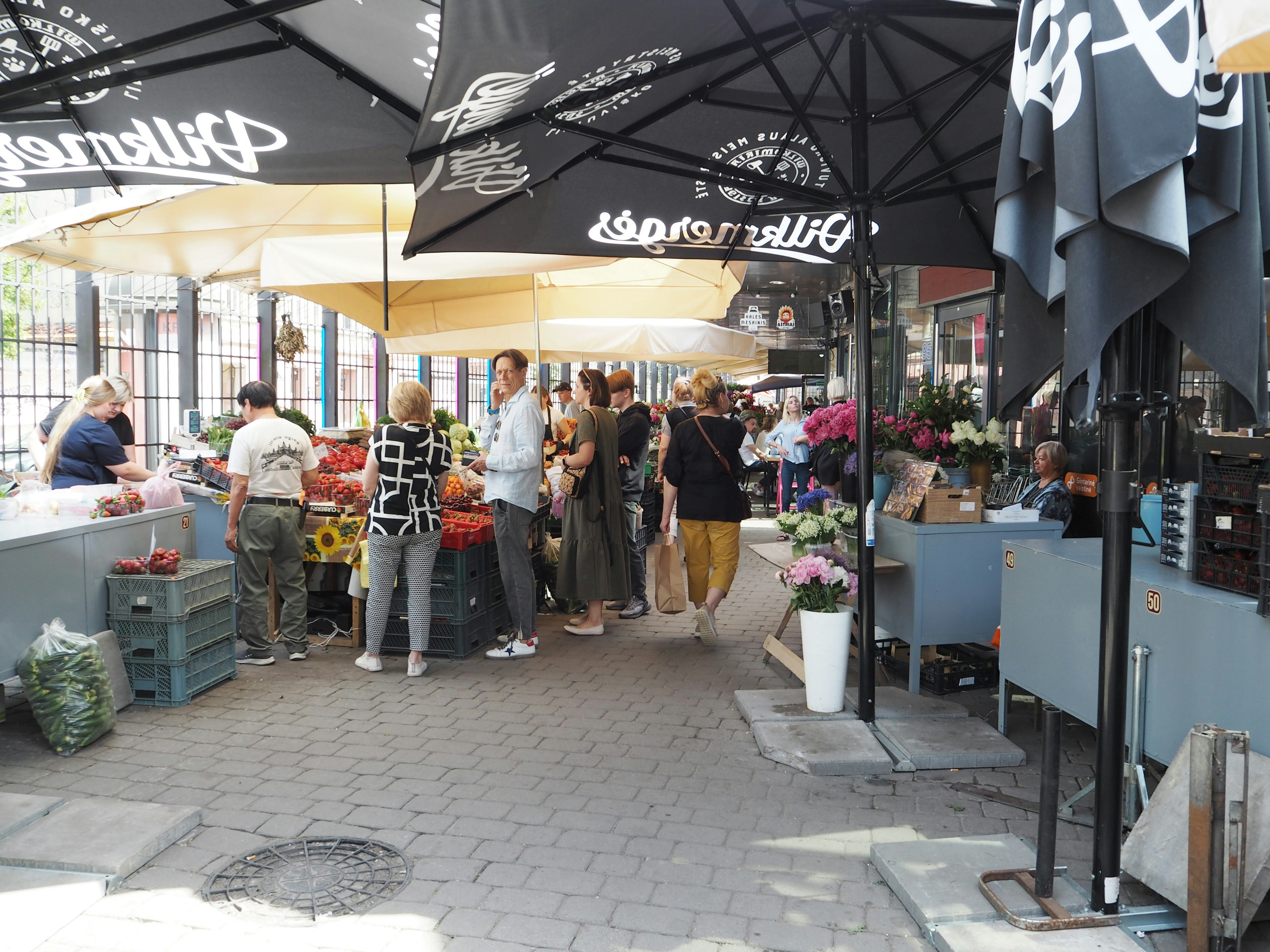 Scène de marché animée avec des fleurs et des légumes en exposition et des gens rassemblés