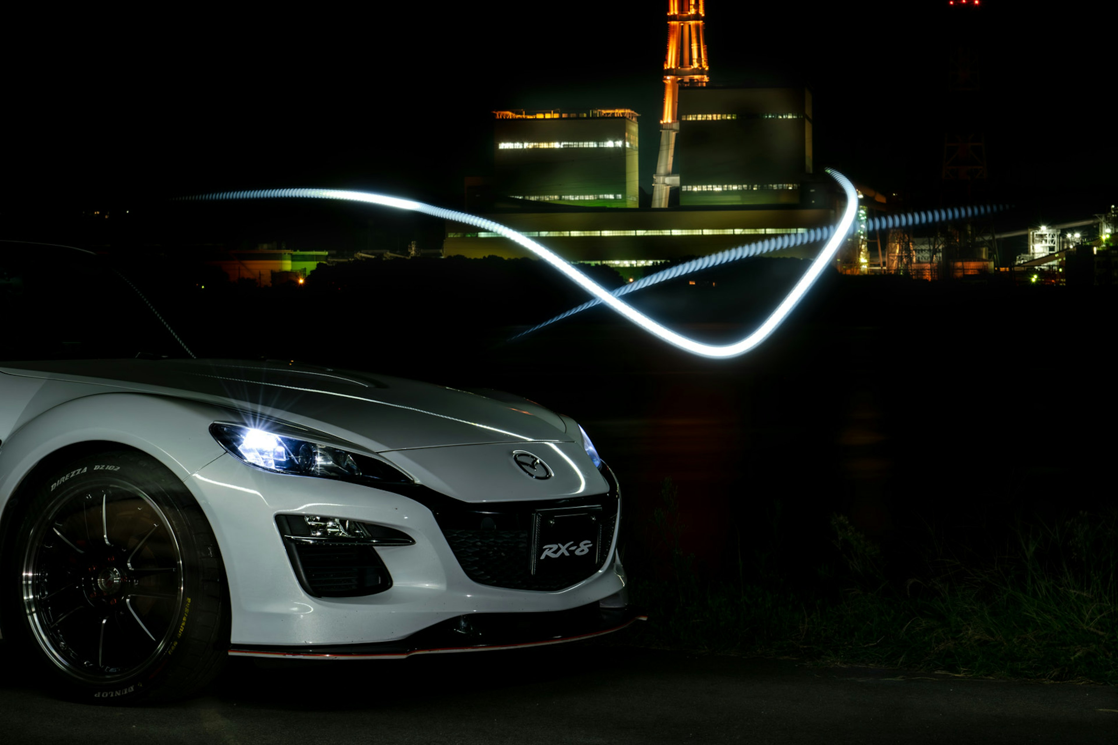 White sports car captured at night with factory lights in the background