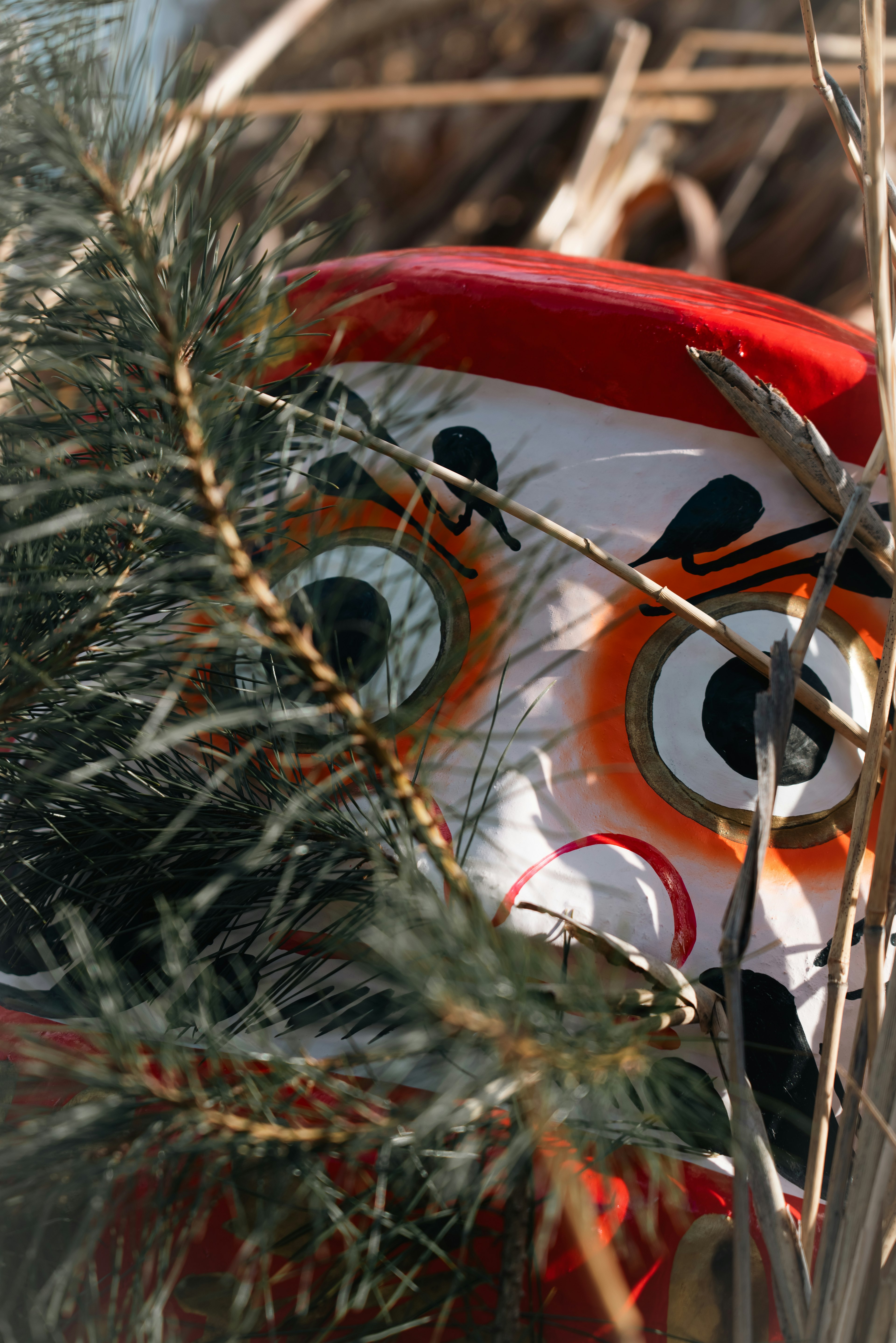 Eine Clownfigur mit rotem Hut und ausdrucksvollem Gesicht, die teilweise im Grün versteckt ist