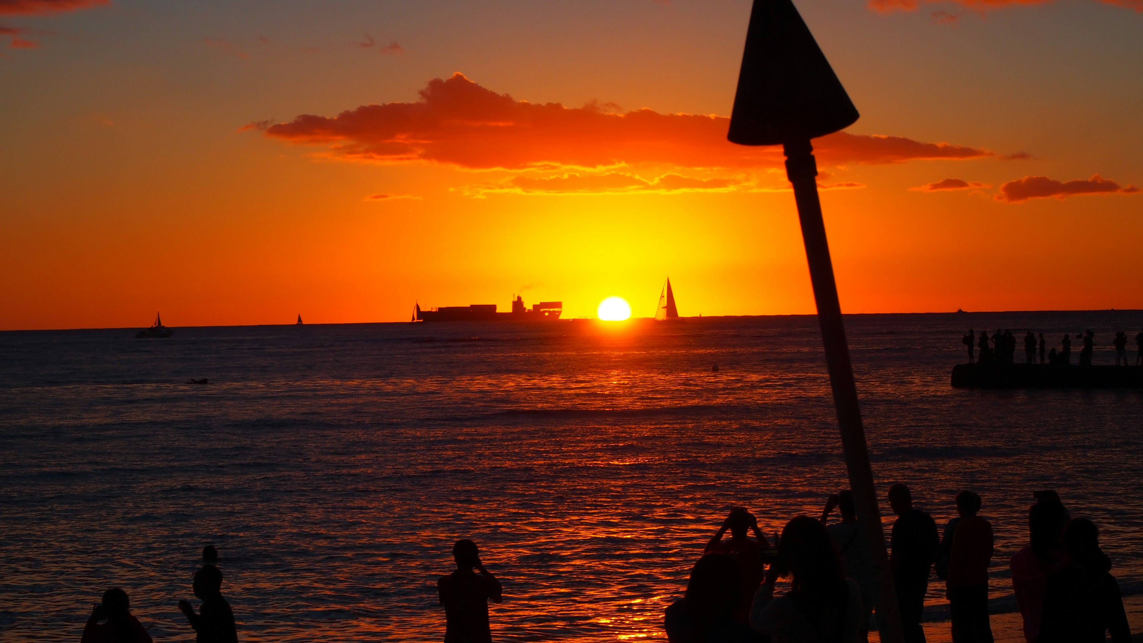 Sunset over the ocean with silhouettes of ships and people