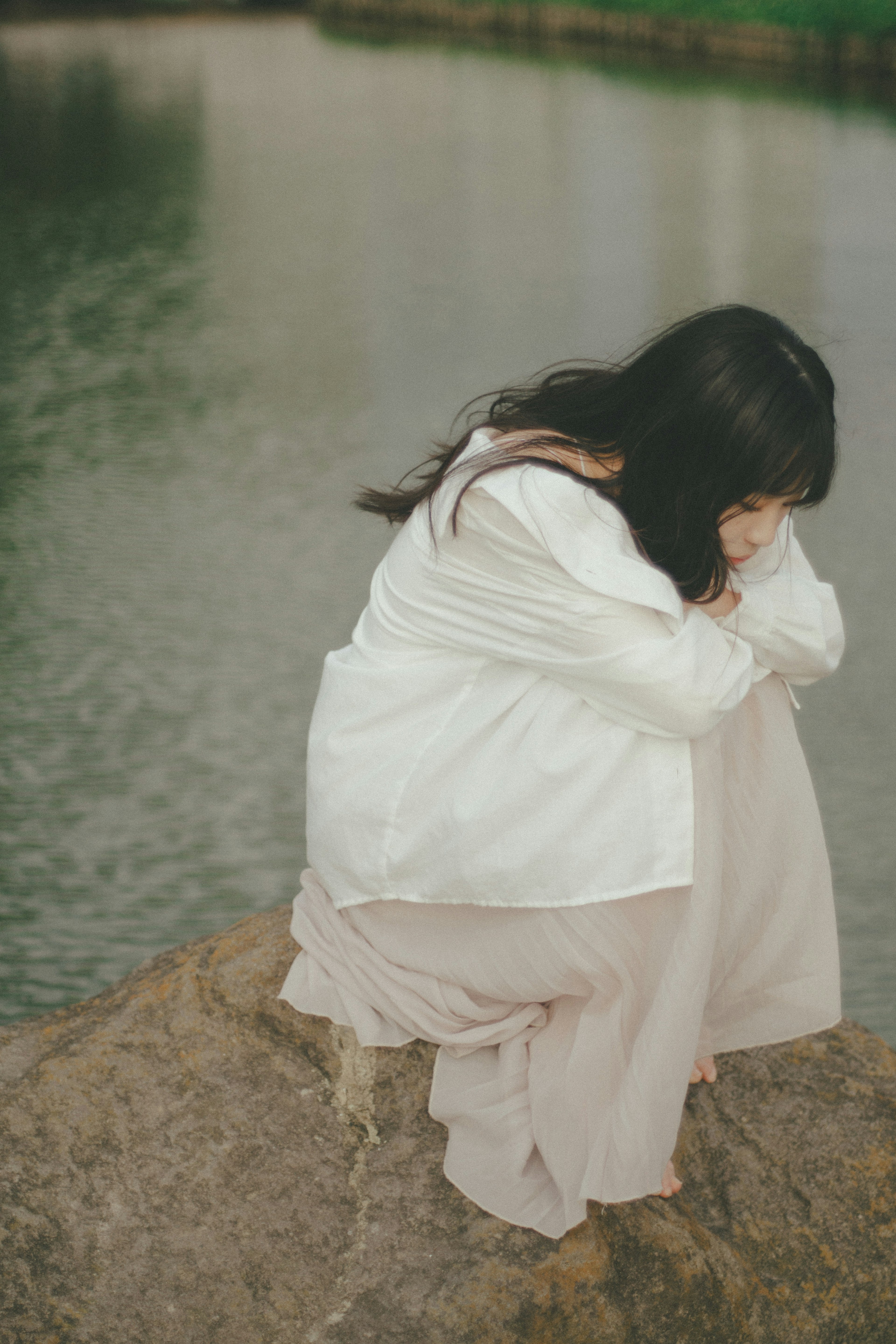 水辺の岩に座る女性 薄い服を着ている 髪は長く流れるよう