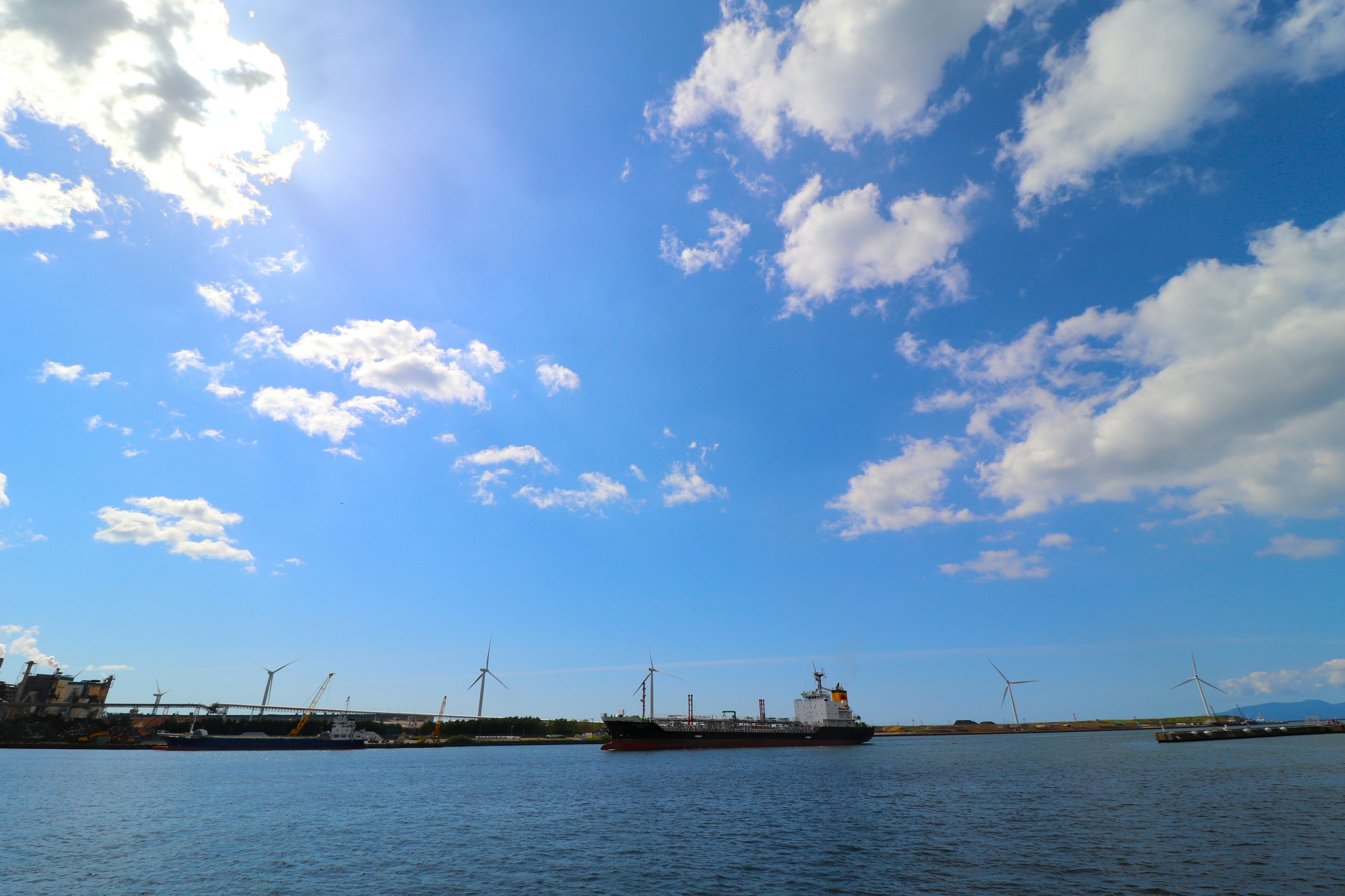 Paisaje marino con barcos anclados bajo un cielo azul brillante y nubes blancas