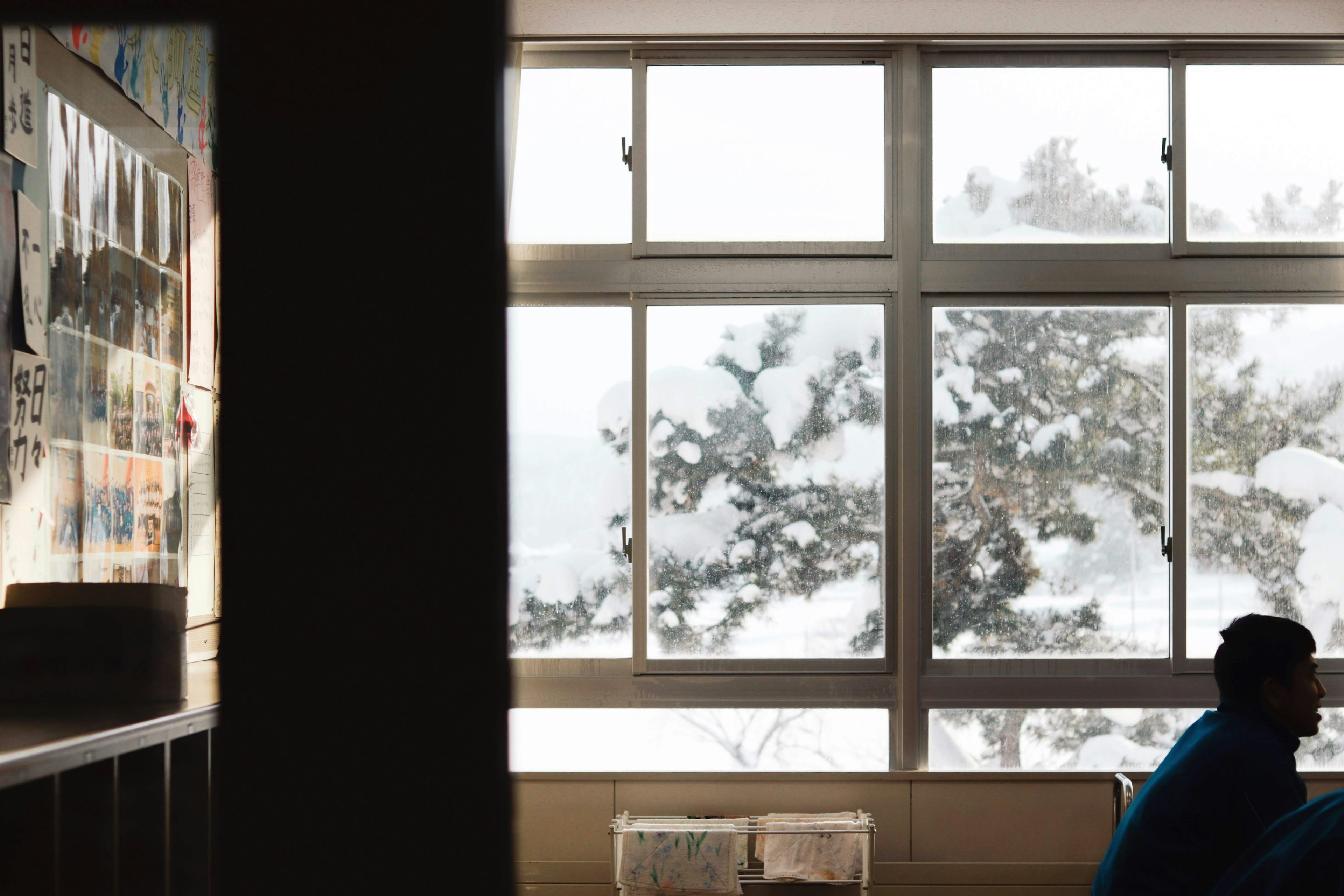 Interior of a classroom with a person gazing out at snow-covered trees through large windows and posters on the wall