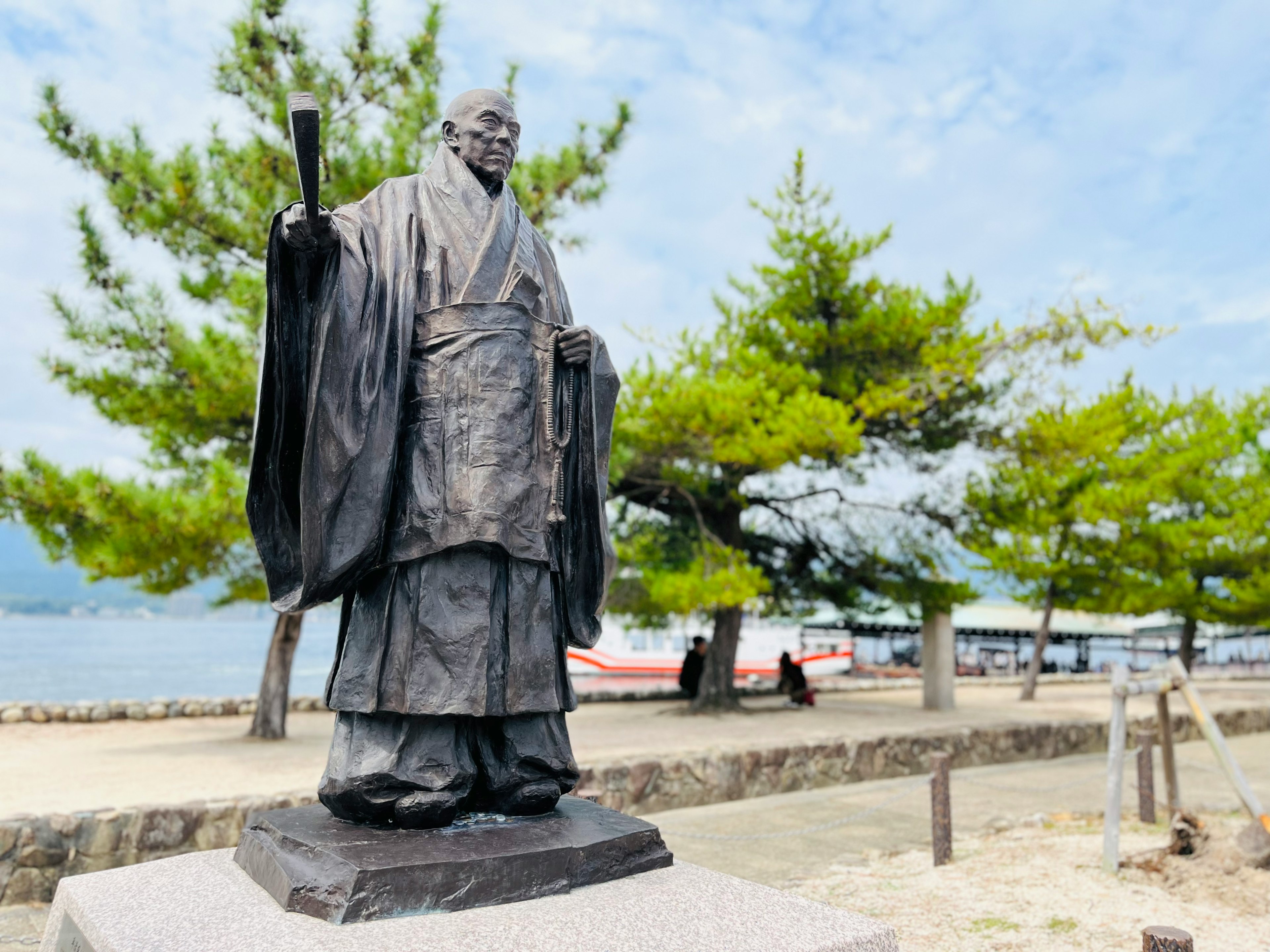 Estatua de bronce de un samurái de pie junto al mar con pinos