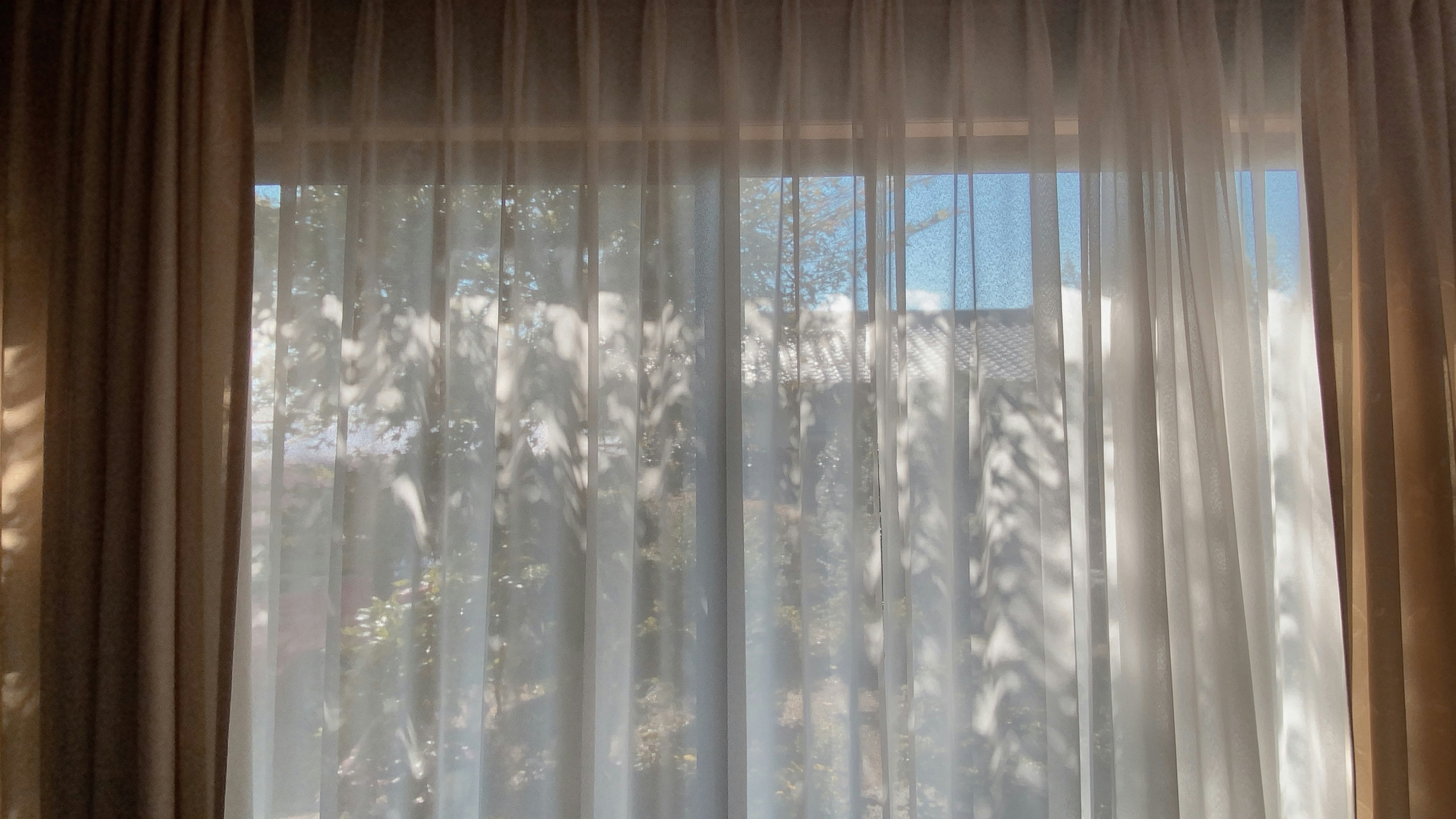 Sheer white curtains revealing blue sky and green foliage