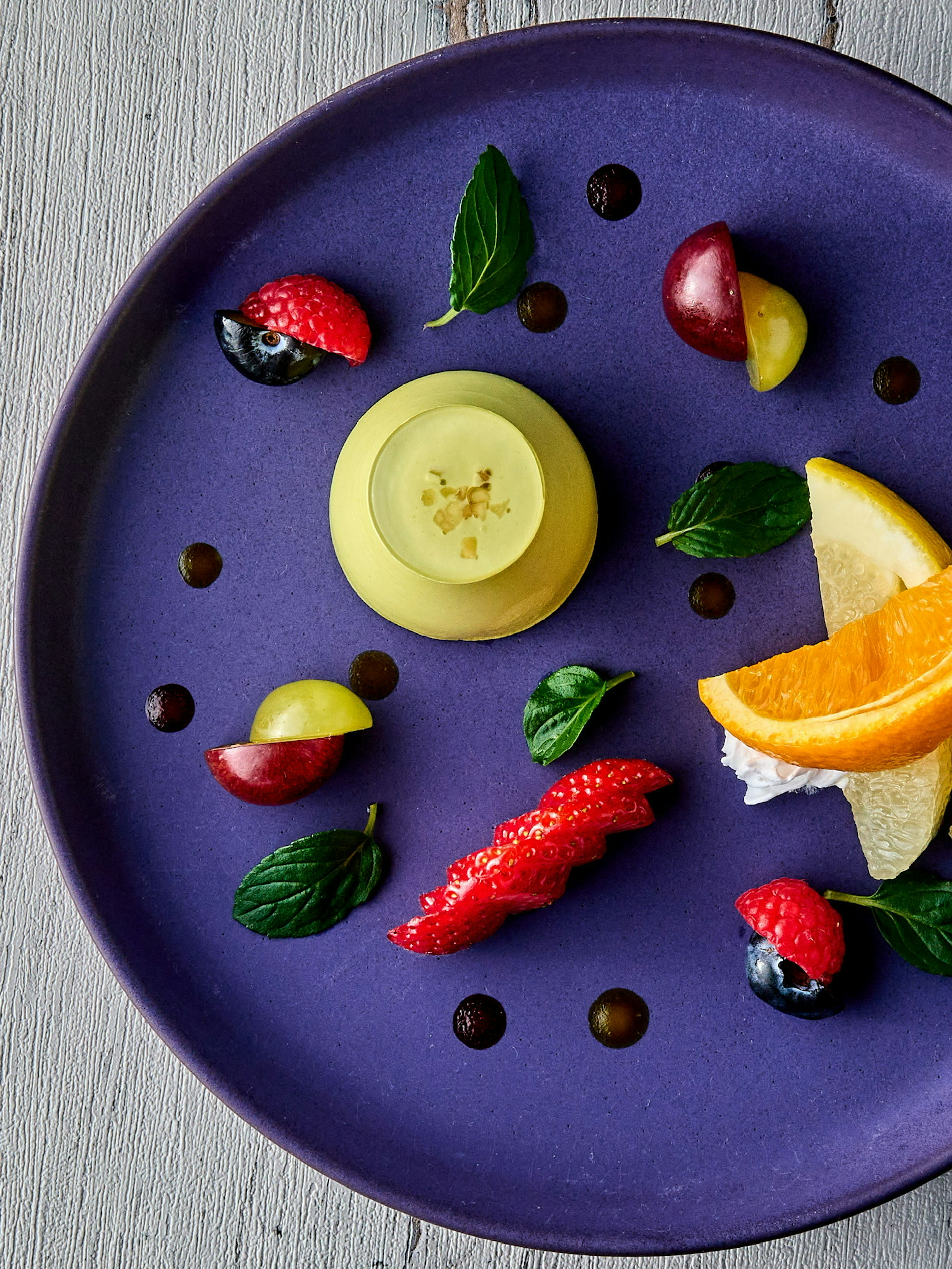 Postre dispuesto en un plato morado con frutas y hojas de menta