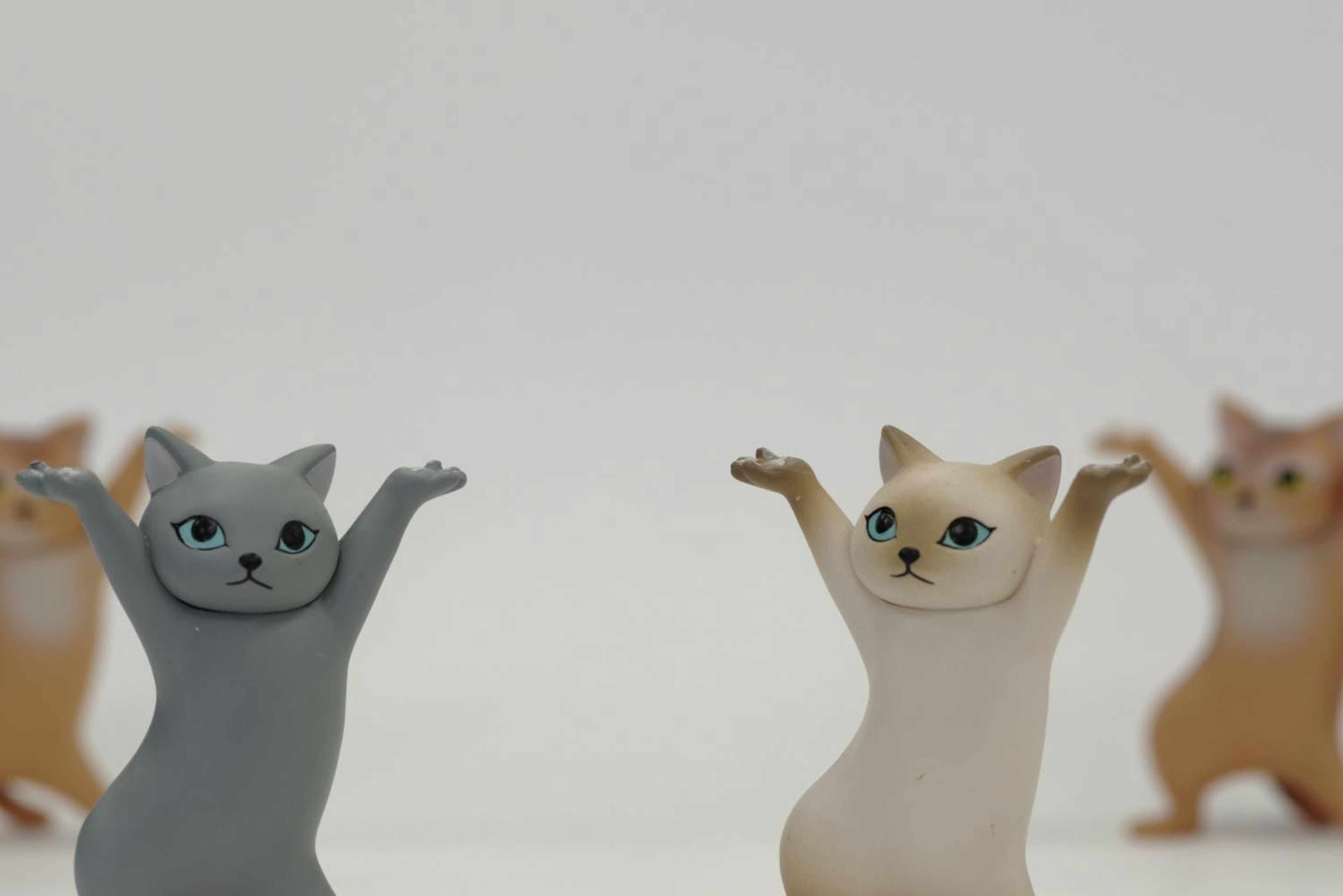 Gray and white cat figurines with raised arms in front of other cat figurines