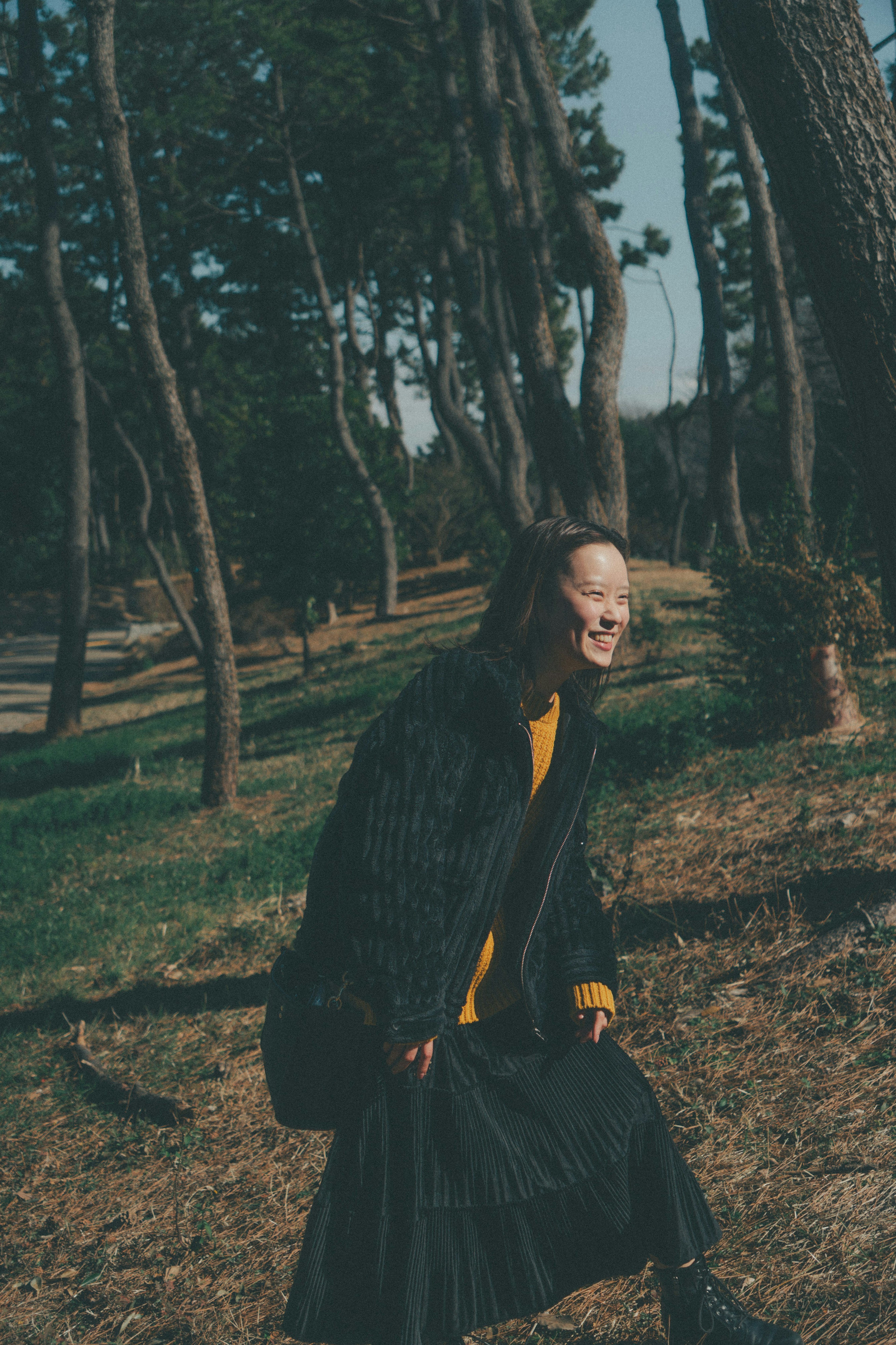 Una donna sorridente in un cappotto nero e un maglione giallo tra gli alberi