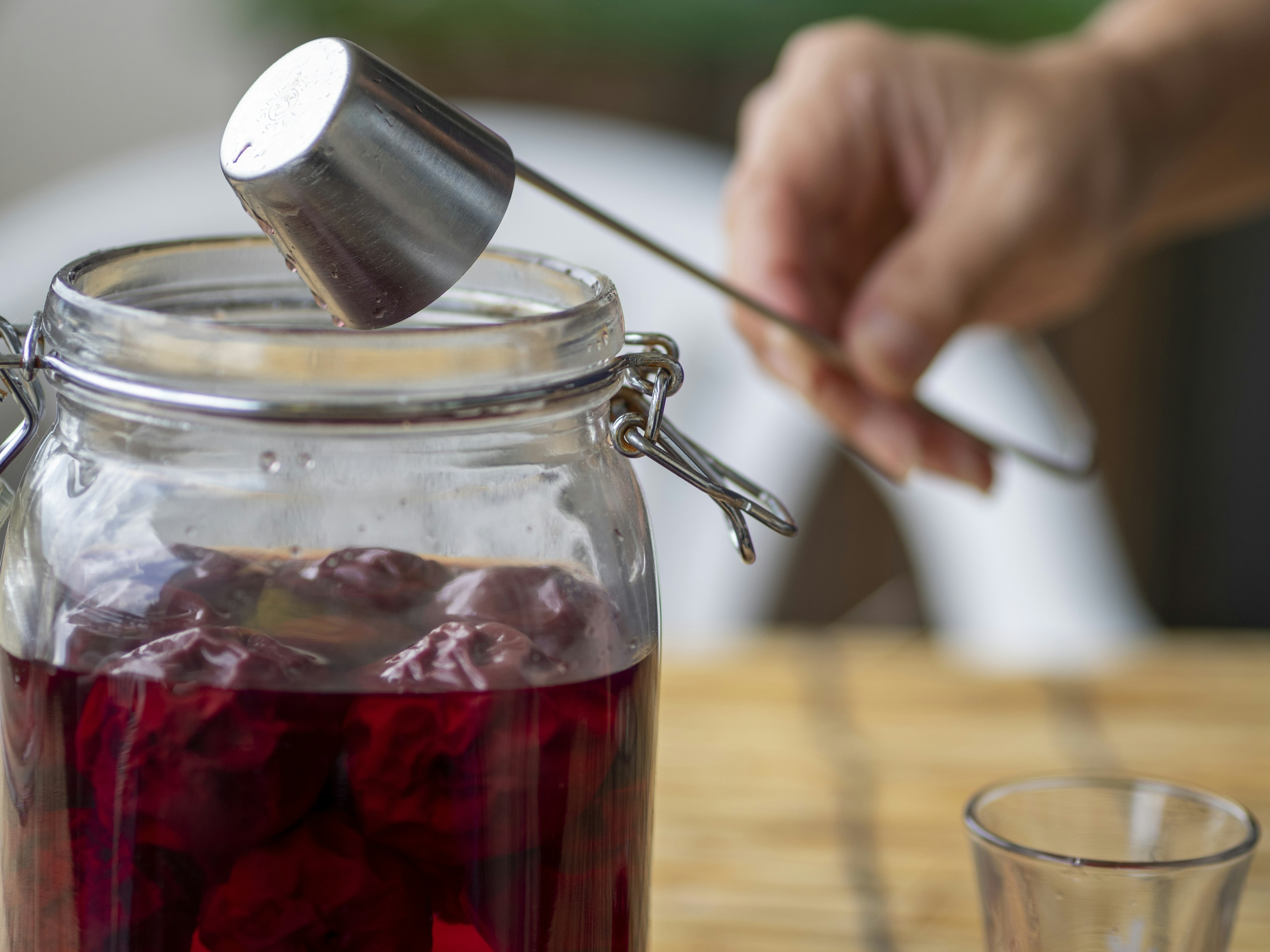 Hand, die einen Messlöffel aus Metall über einem Glas mit roter Flüssigkeit hält