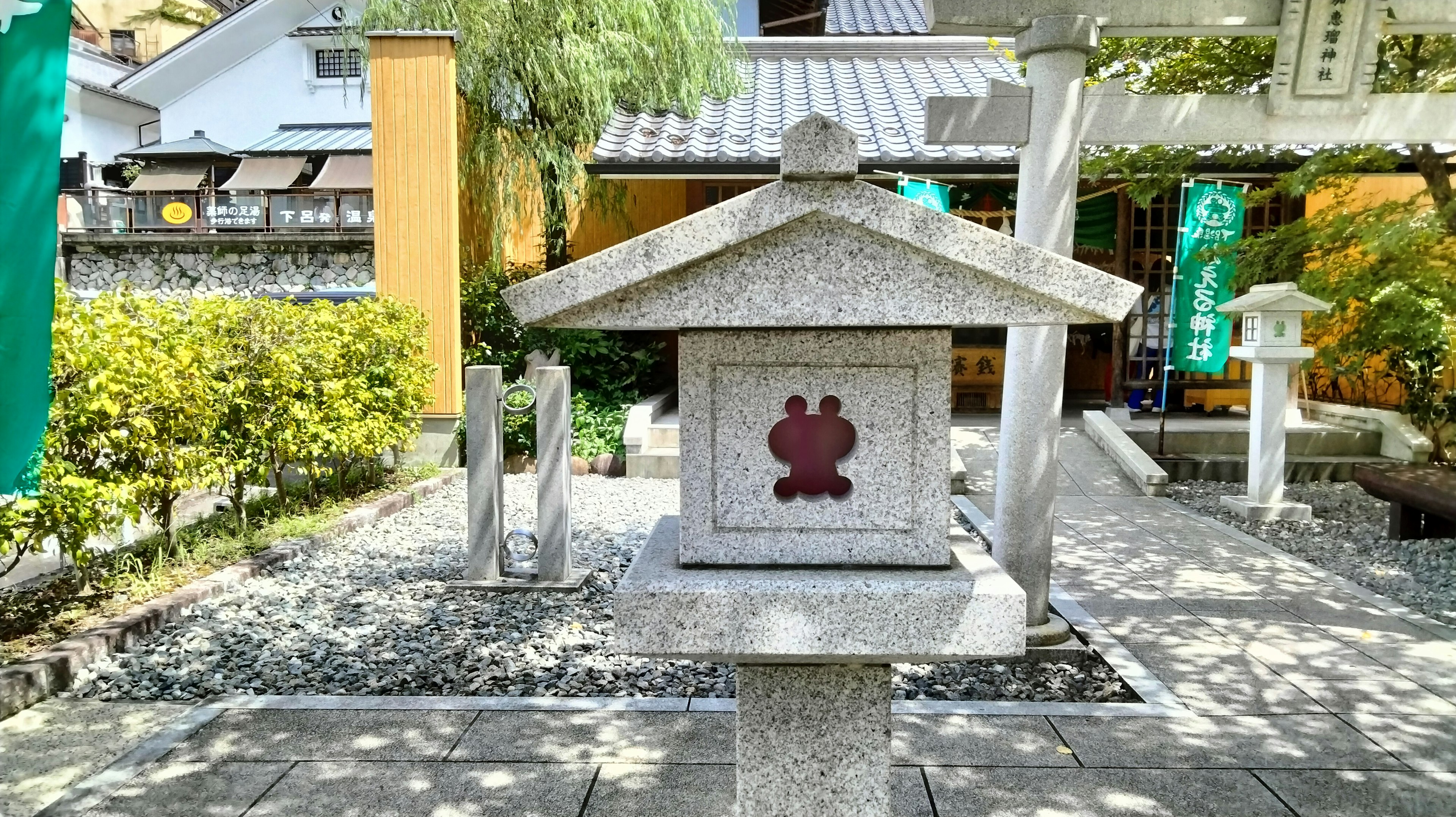 Steinlaterne an einem Schrein mit rotem Schildkröten-Symbol umgeben von einem üppigen Garten