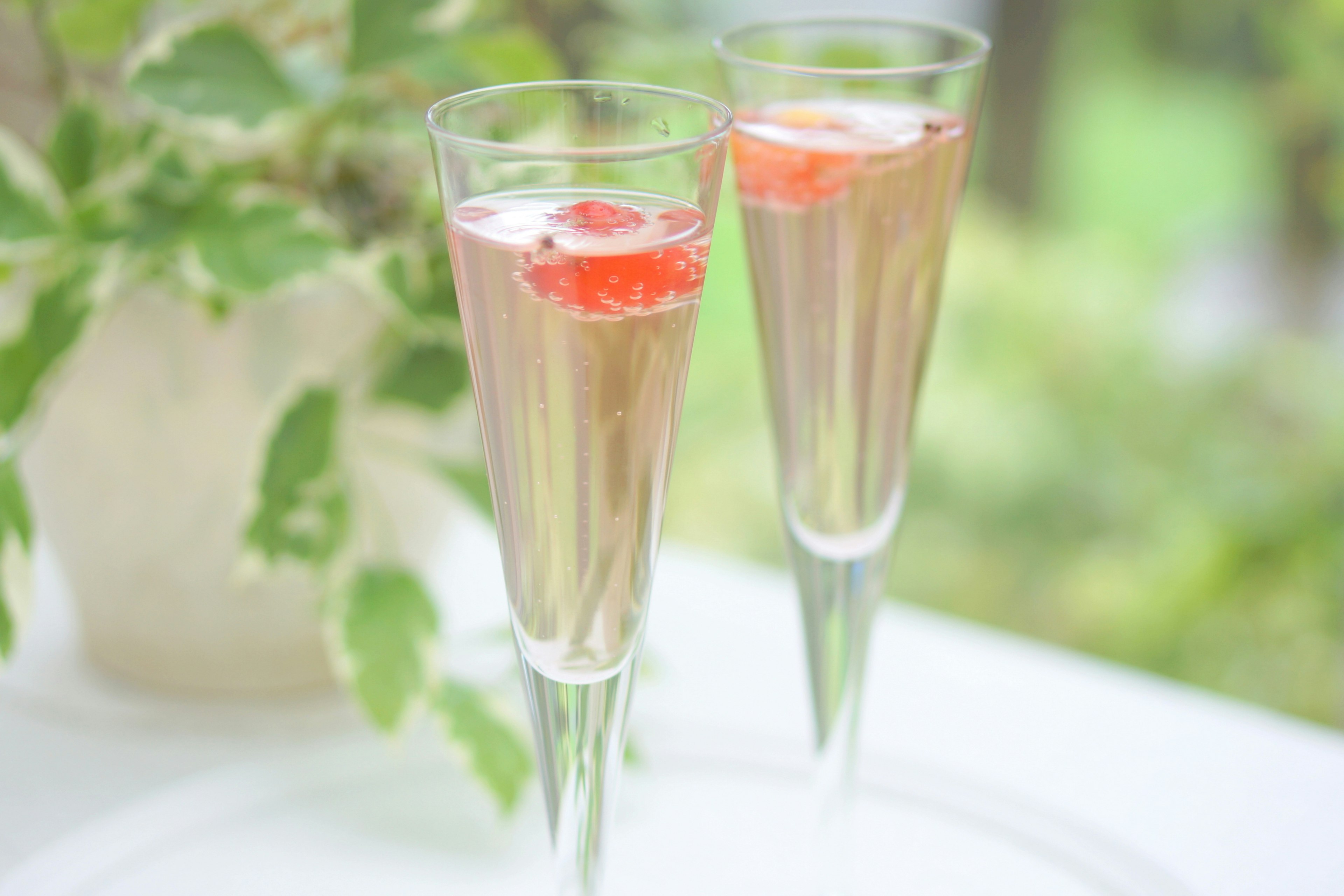 Two champagne glasses with pink liquid and a red fruit garnish against a green background