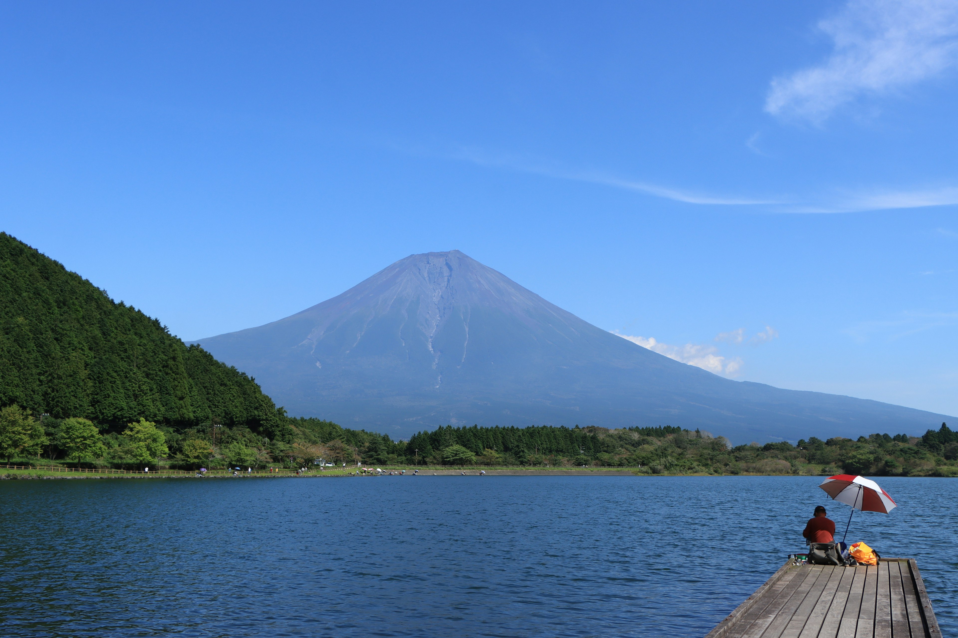 Vue pittoresque du mont Fuji avec un lac et des personnes assises sur un quai en bois