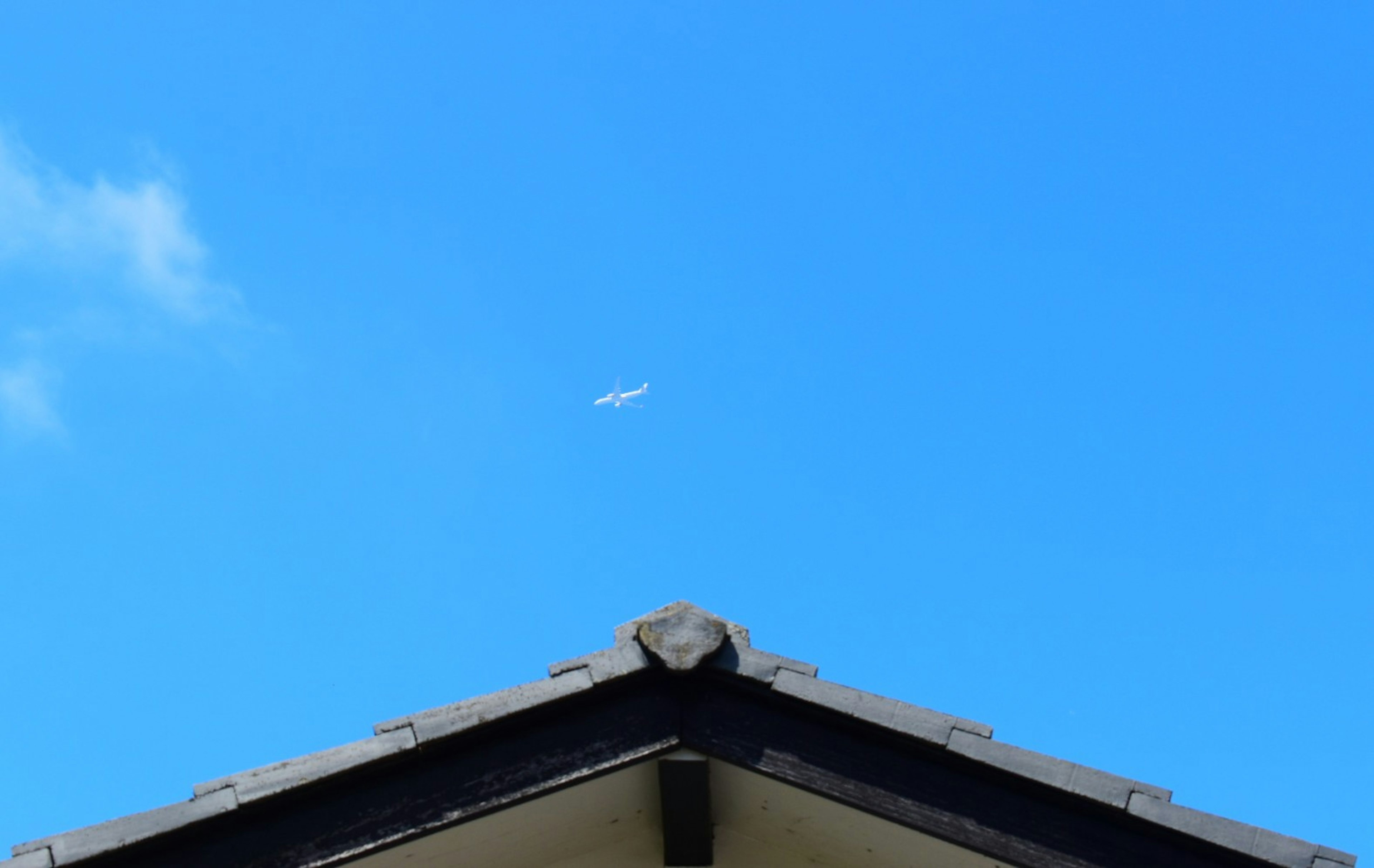 Small airplane in the blue sky above a building roof