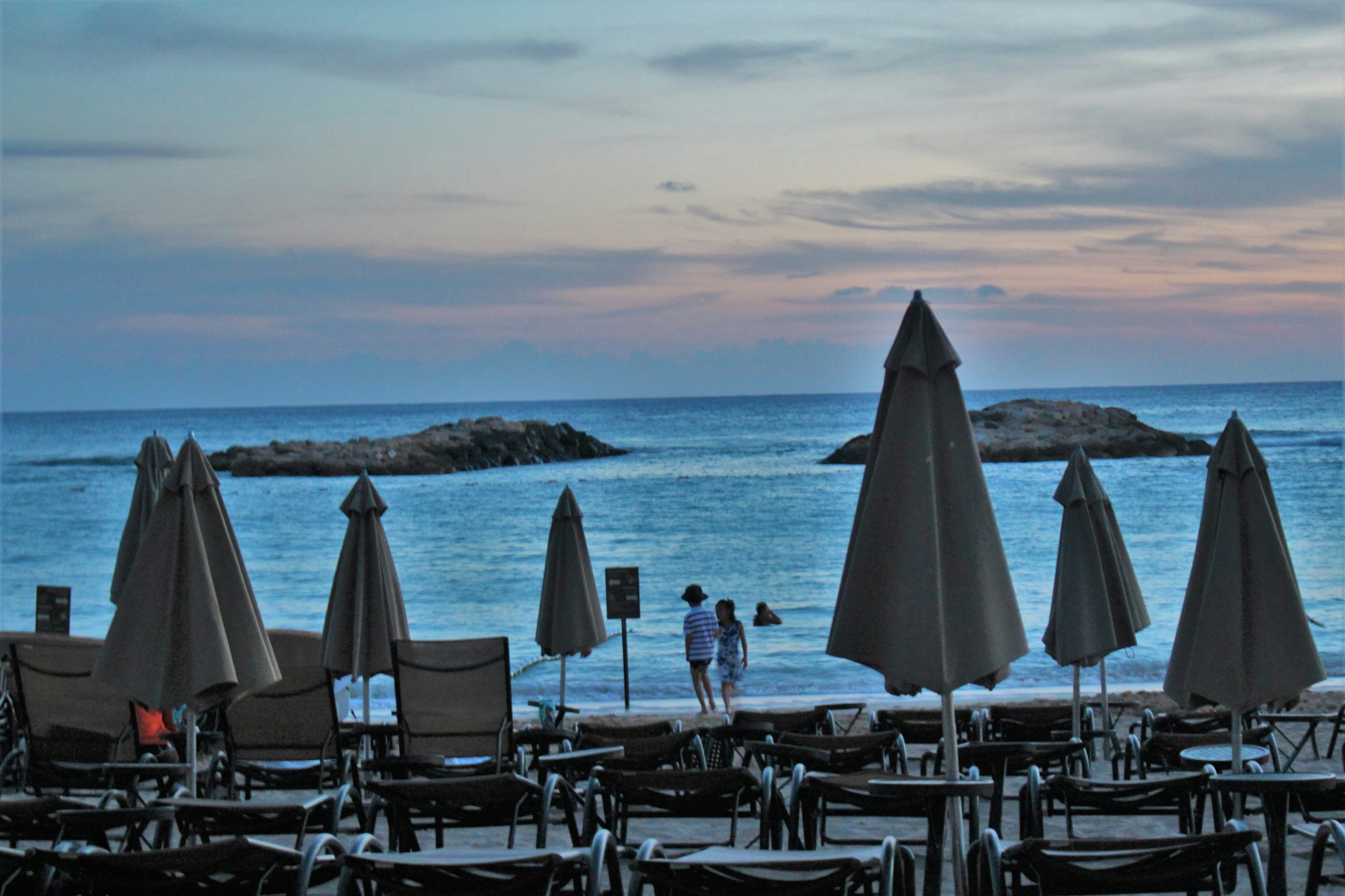 Escena de playa con sombrillas y sillas con vista al mar y rocas al atardecer