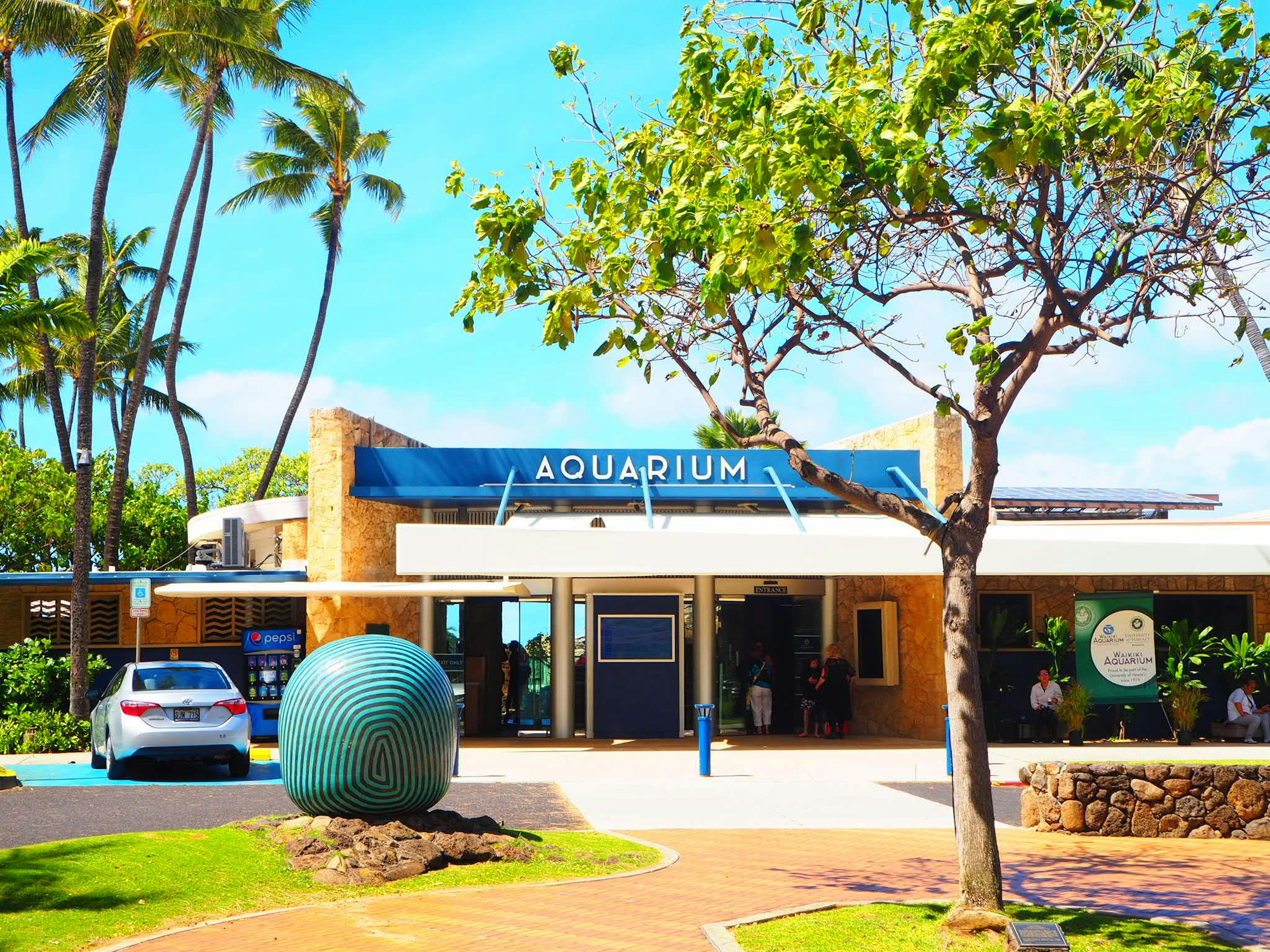 Bâtiment de l'aquarium sous un ciel bleu et des palmiers avec une sculpture ronde