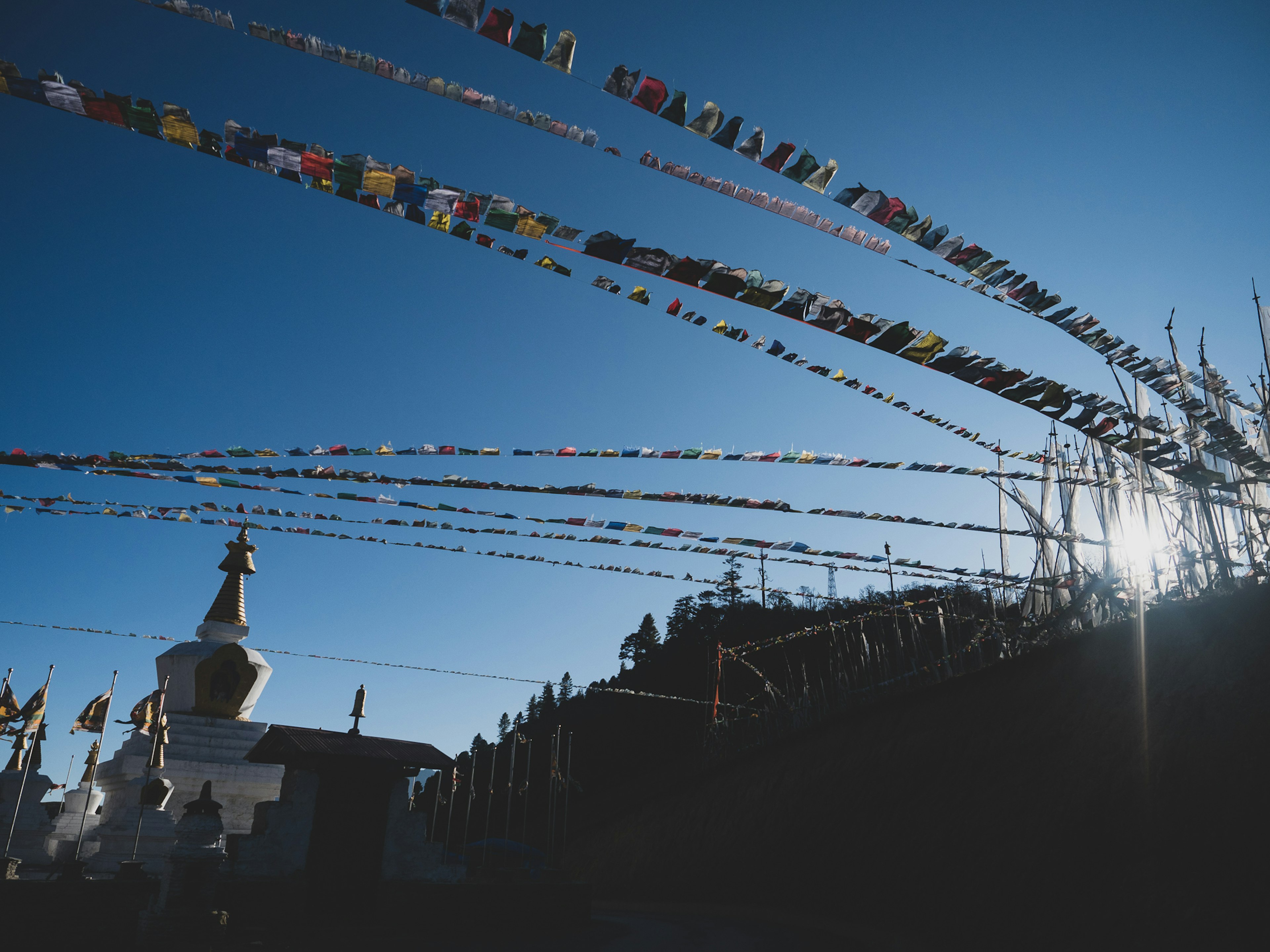 Colorful prayer flags stretching across a blue sky with a stupa in silhouette