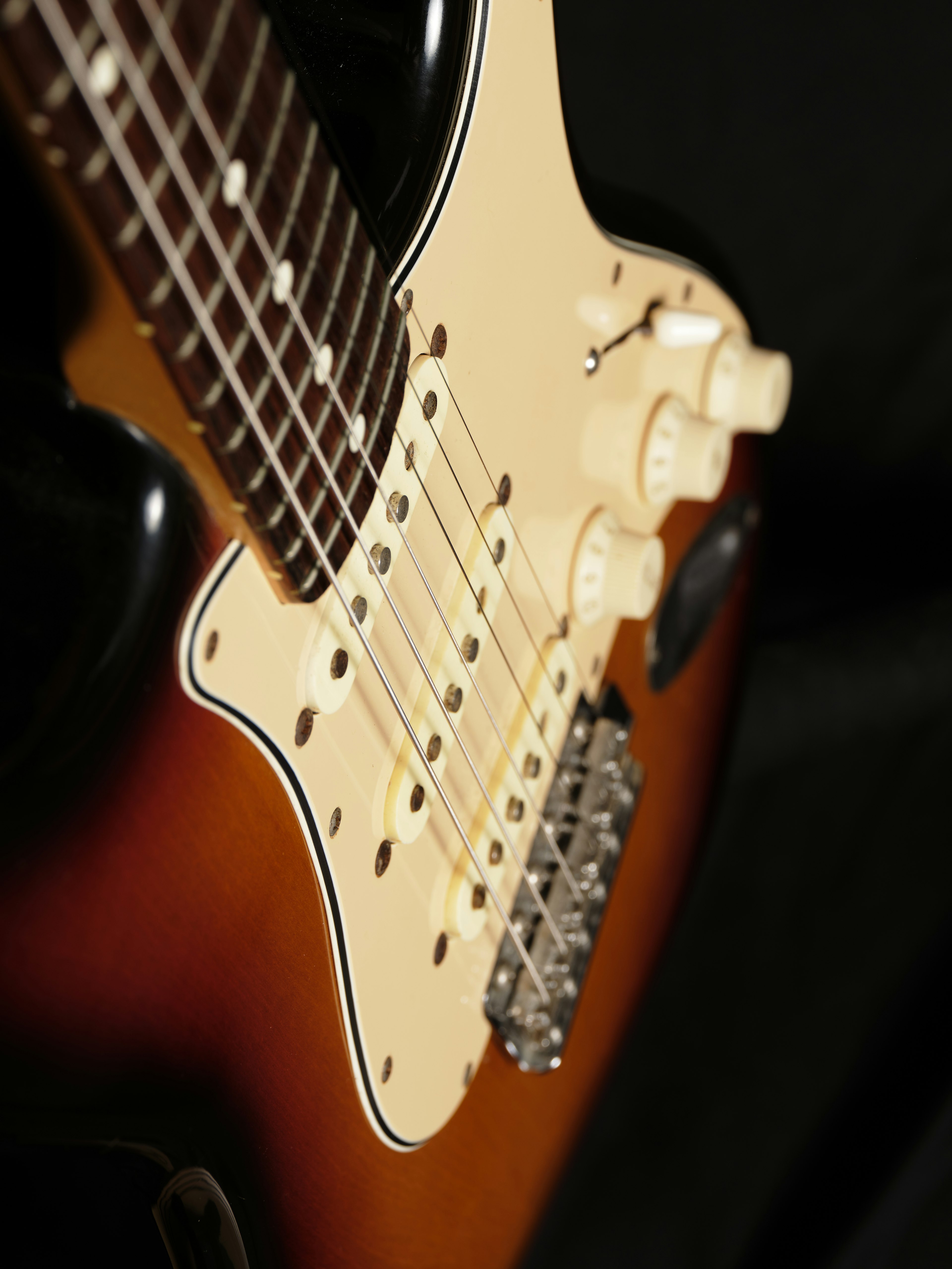 Gambar close-up gitar listrik dengan finishing sunburst dan pickup serta knob yang terlihat