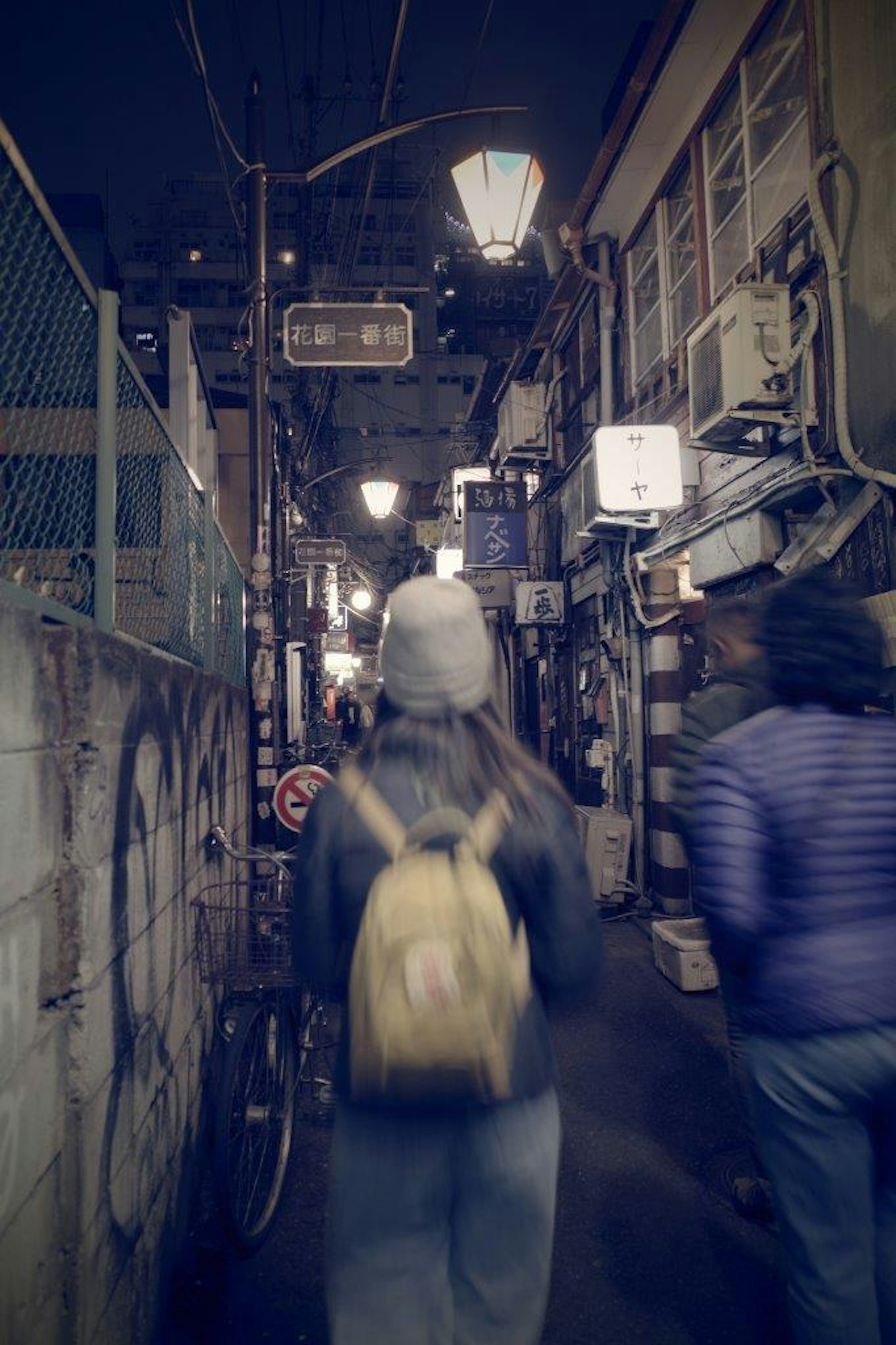 Vicolo stretto con persone che camminano di notte e lampioni vintage