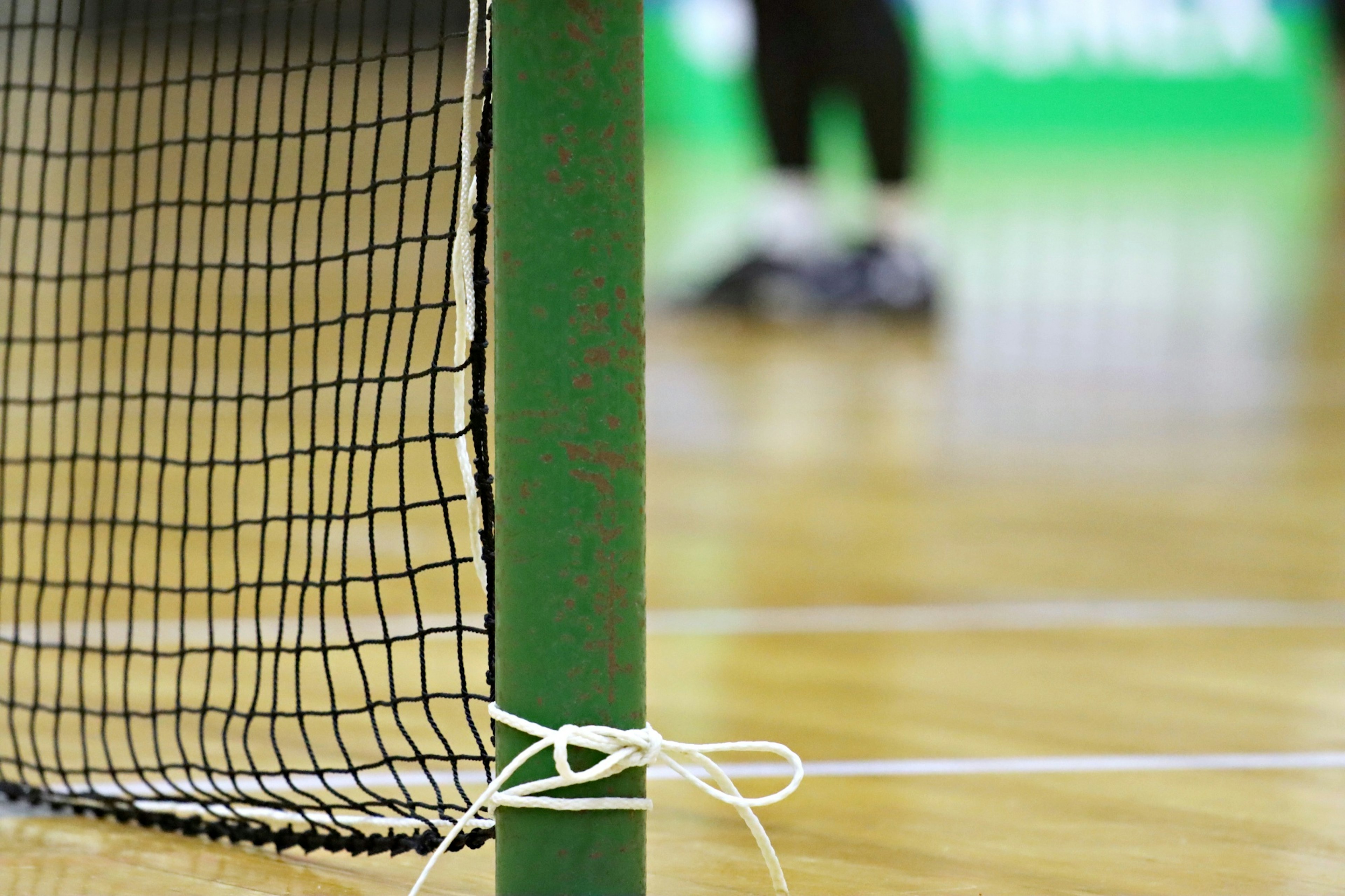 Primo piano di un palo di rete da badminton con un giocatore sfocato sullo sfondo