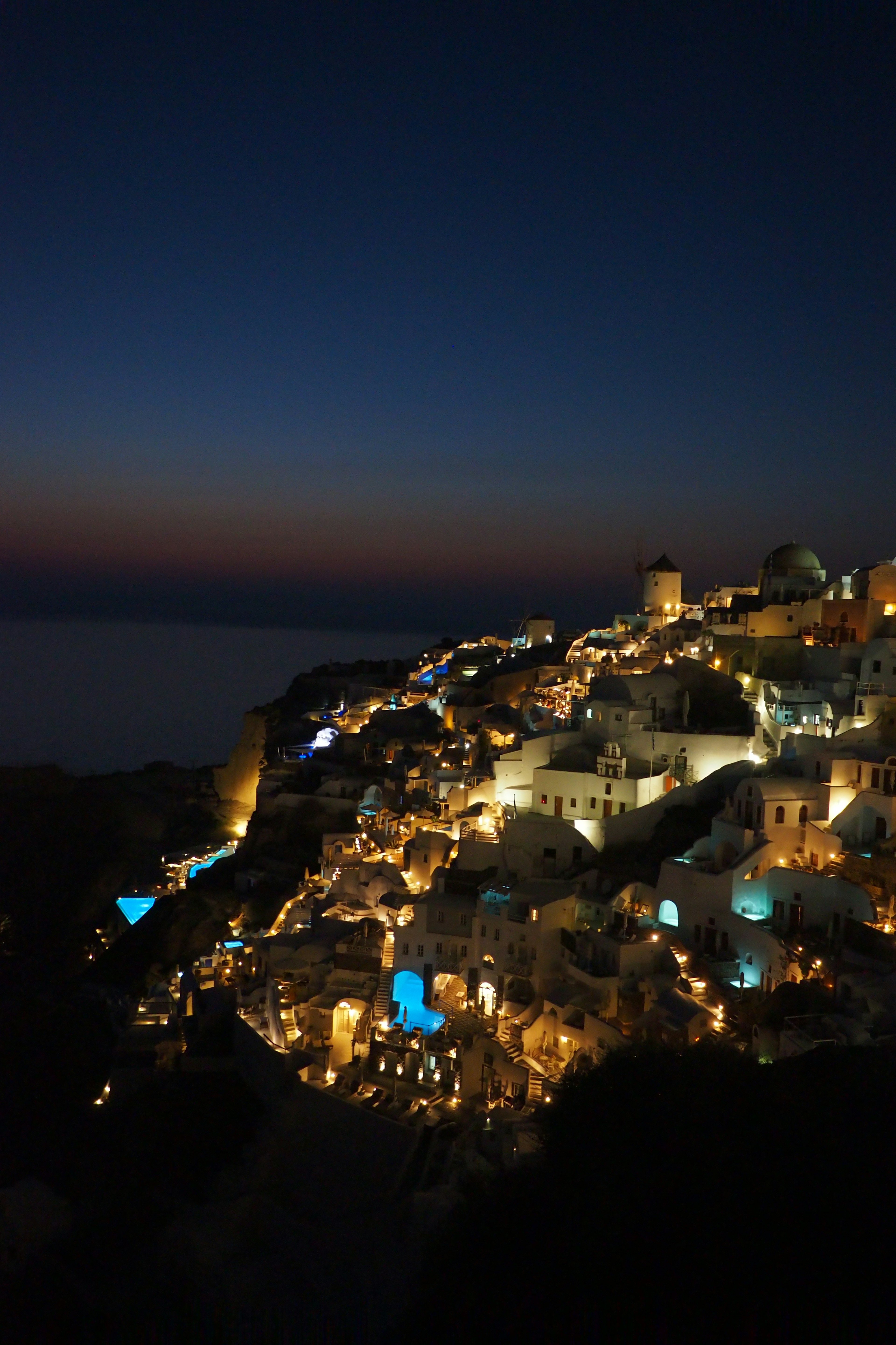 Schöne Nachtansicht von Santorin mit beleuchteten Gebäuden und blauem Meer