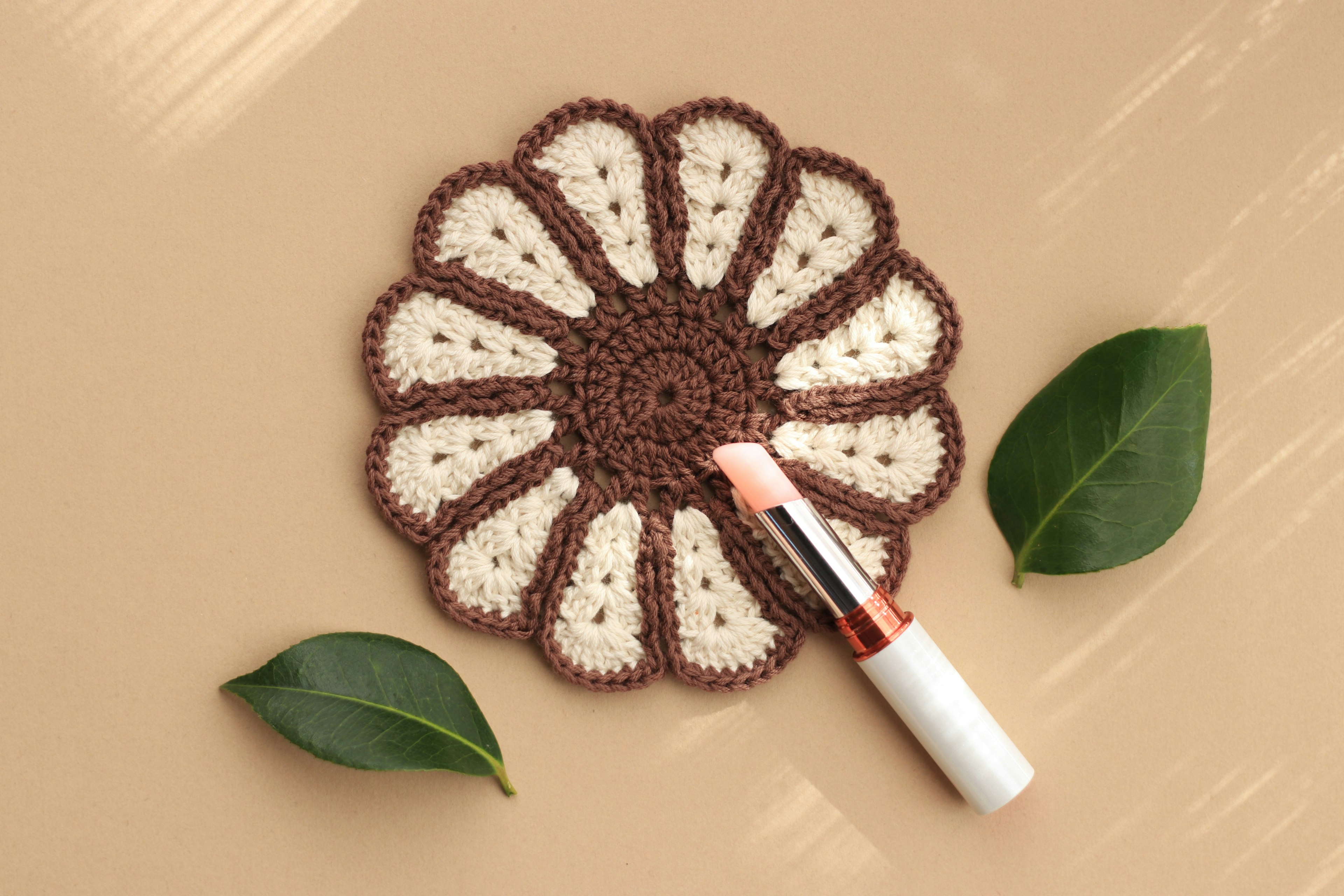 Un sous-verre en forme de fleur de couleur marron et crème avec un rouge à lèvres à côté