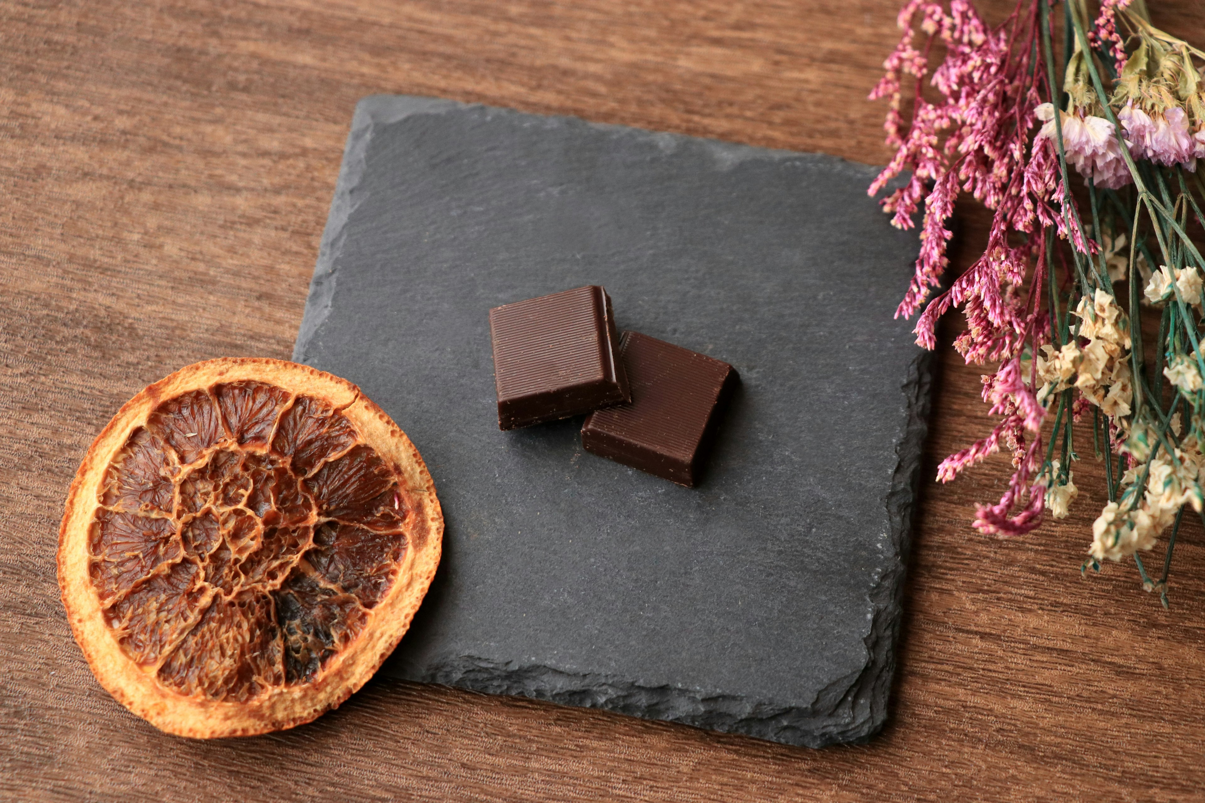 Carrés de chocolat noir sur une assiette en ardoise noire à côté d'une tranche d'orange séchée