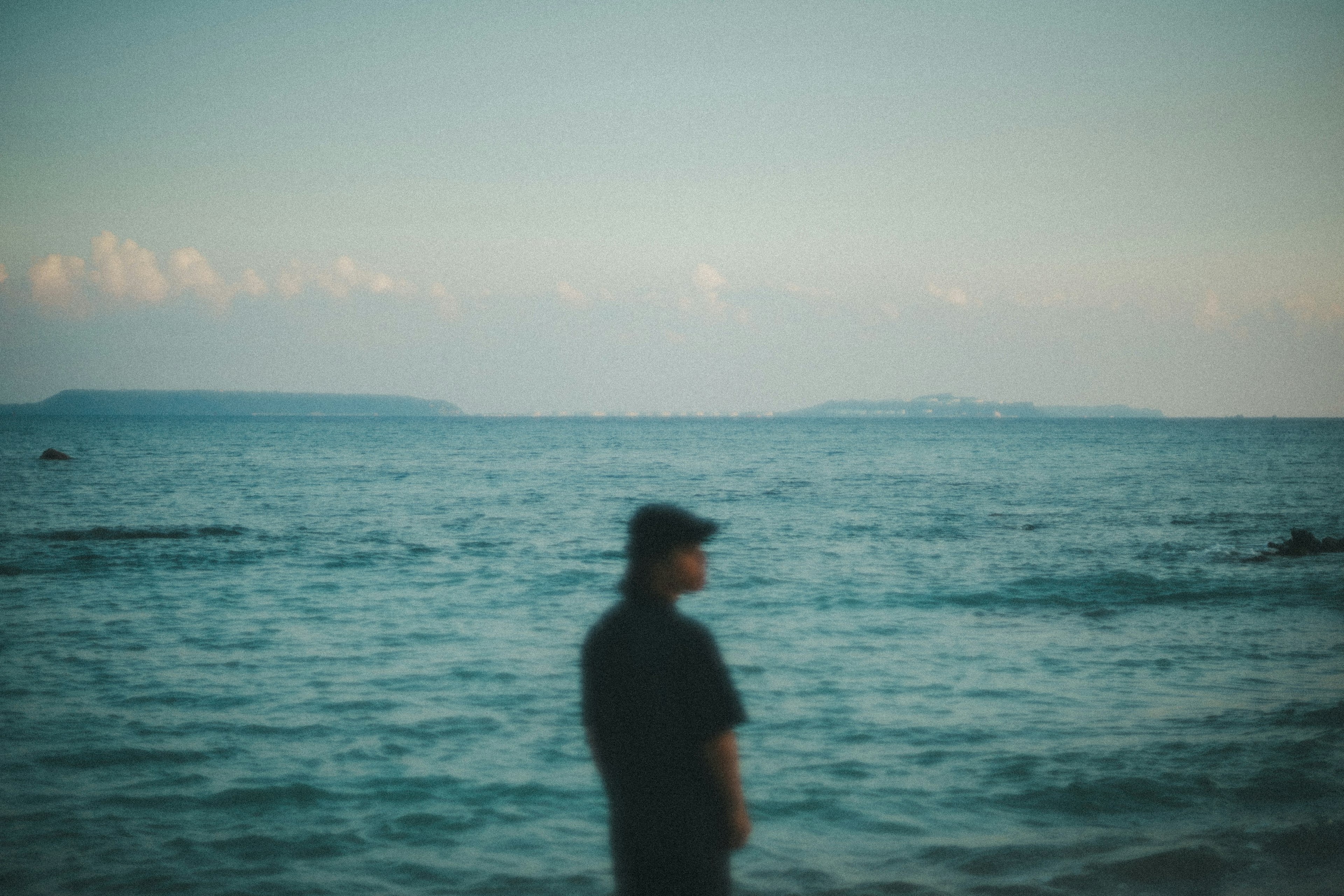 해변에 서 있는 사람의 실루엣과 파란 바다와 하늘 배경