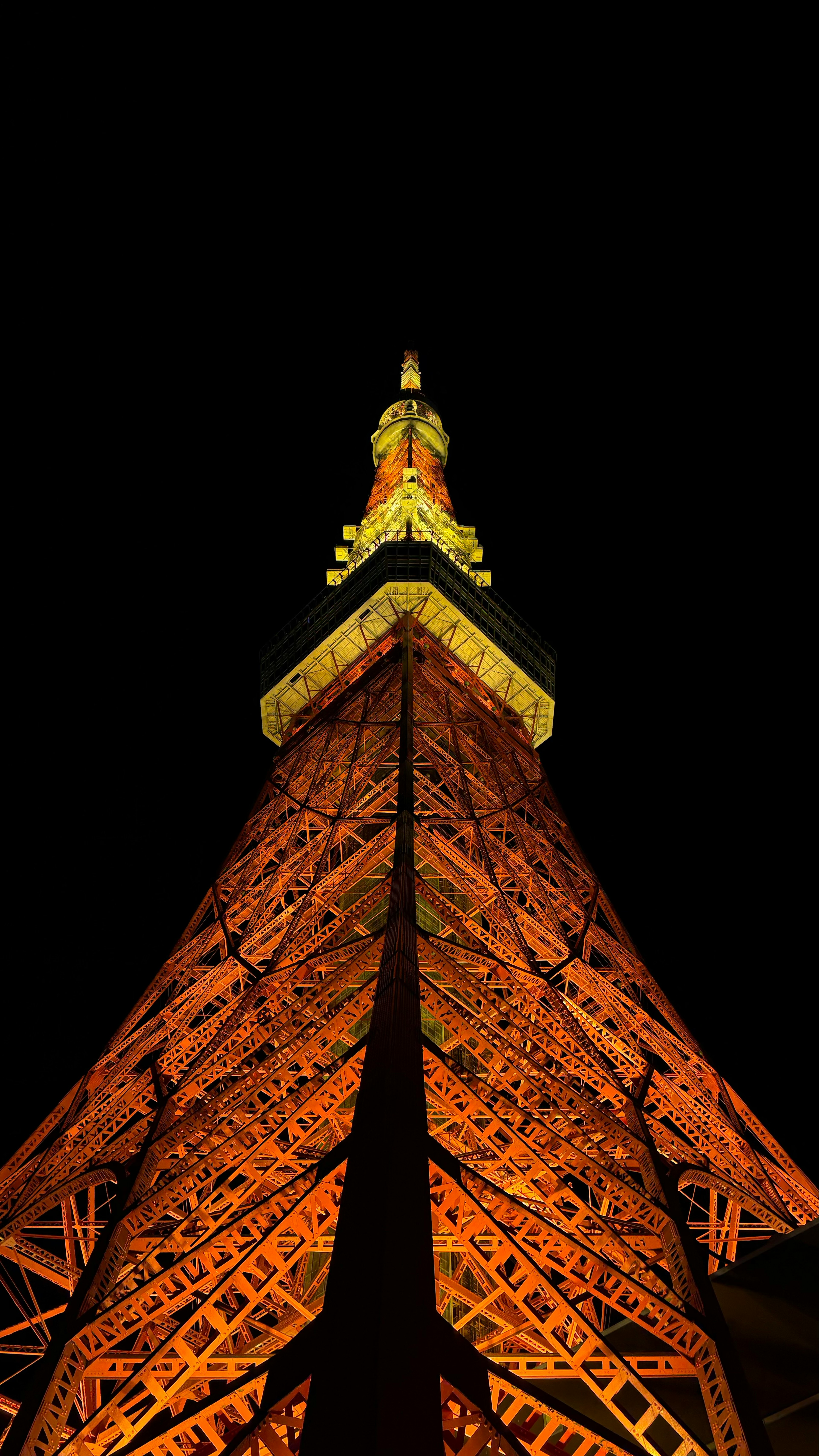 Foto des Tokyo Tower bei Nacht von unten gesehen Helle orangefarbene Stahlstruktur und beleuchtete Spitze sind markant