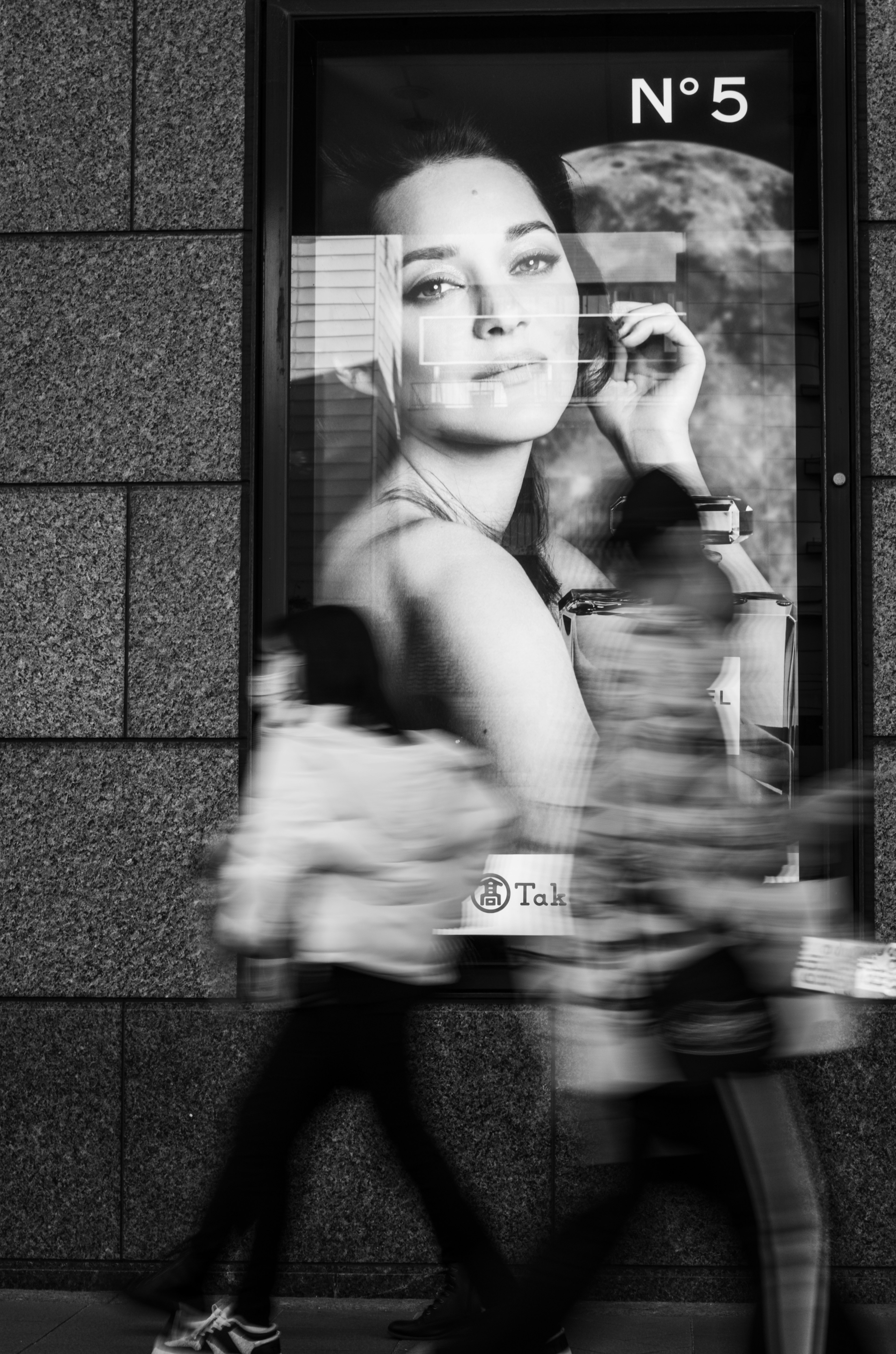 Contraste entre des piétons passant devant un grand portrait d'une femme