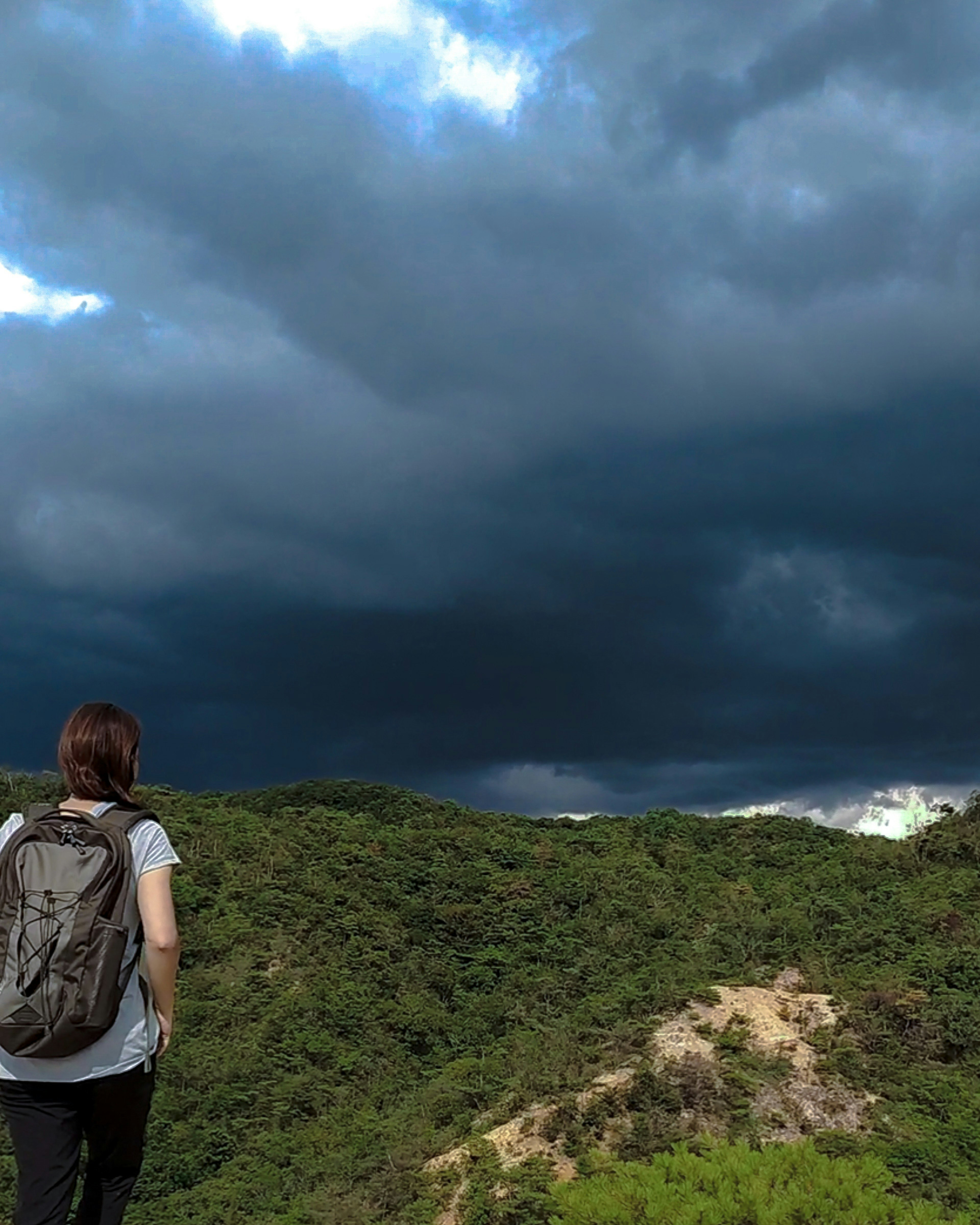 女人凝視著有黑雲和綠色山丘的山地風景