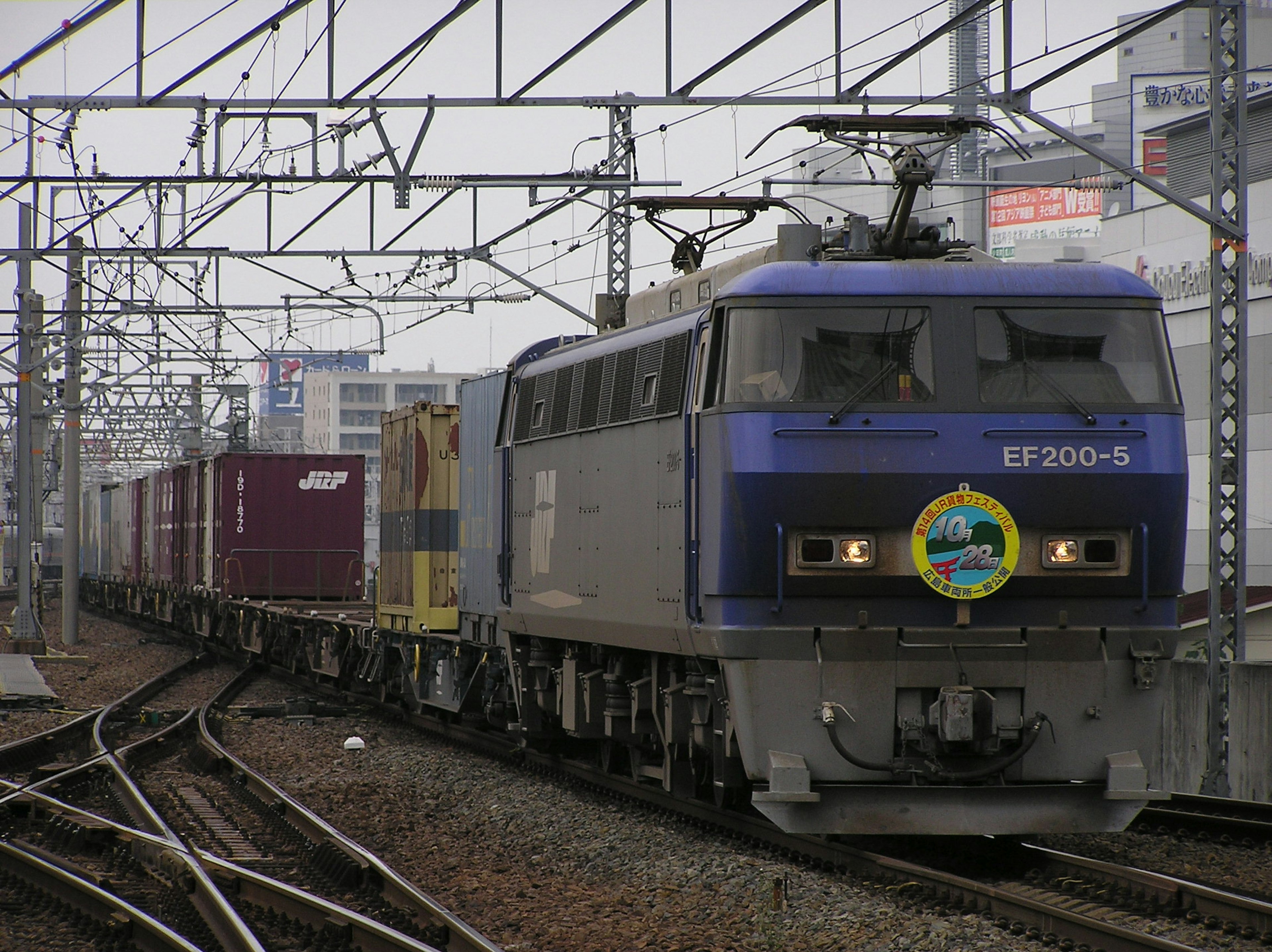 A blue freight train moving along tracks with a cityscape in the background