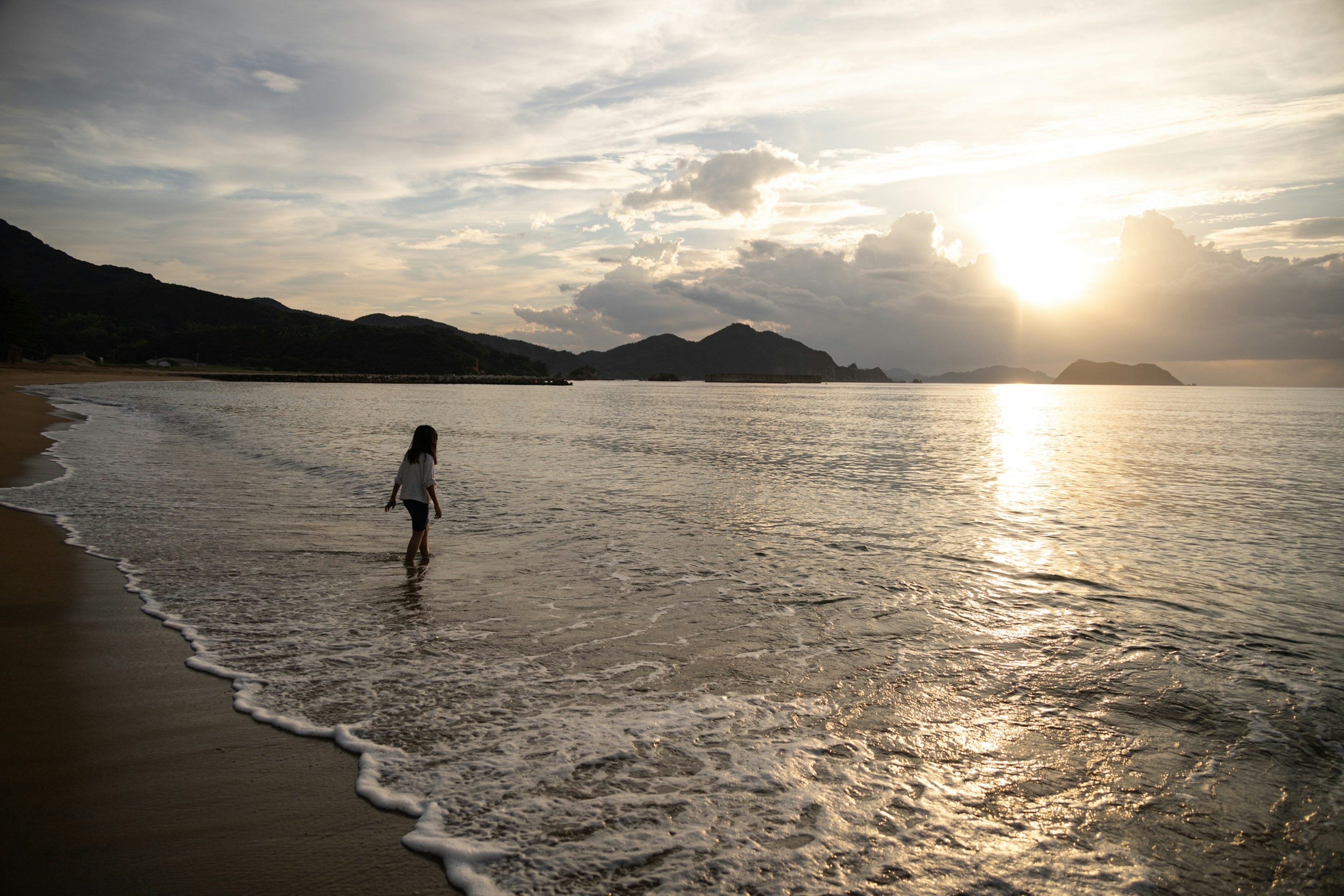 Una mujer caminando por la playa con una hermosa puesta de sol