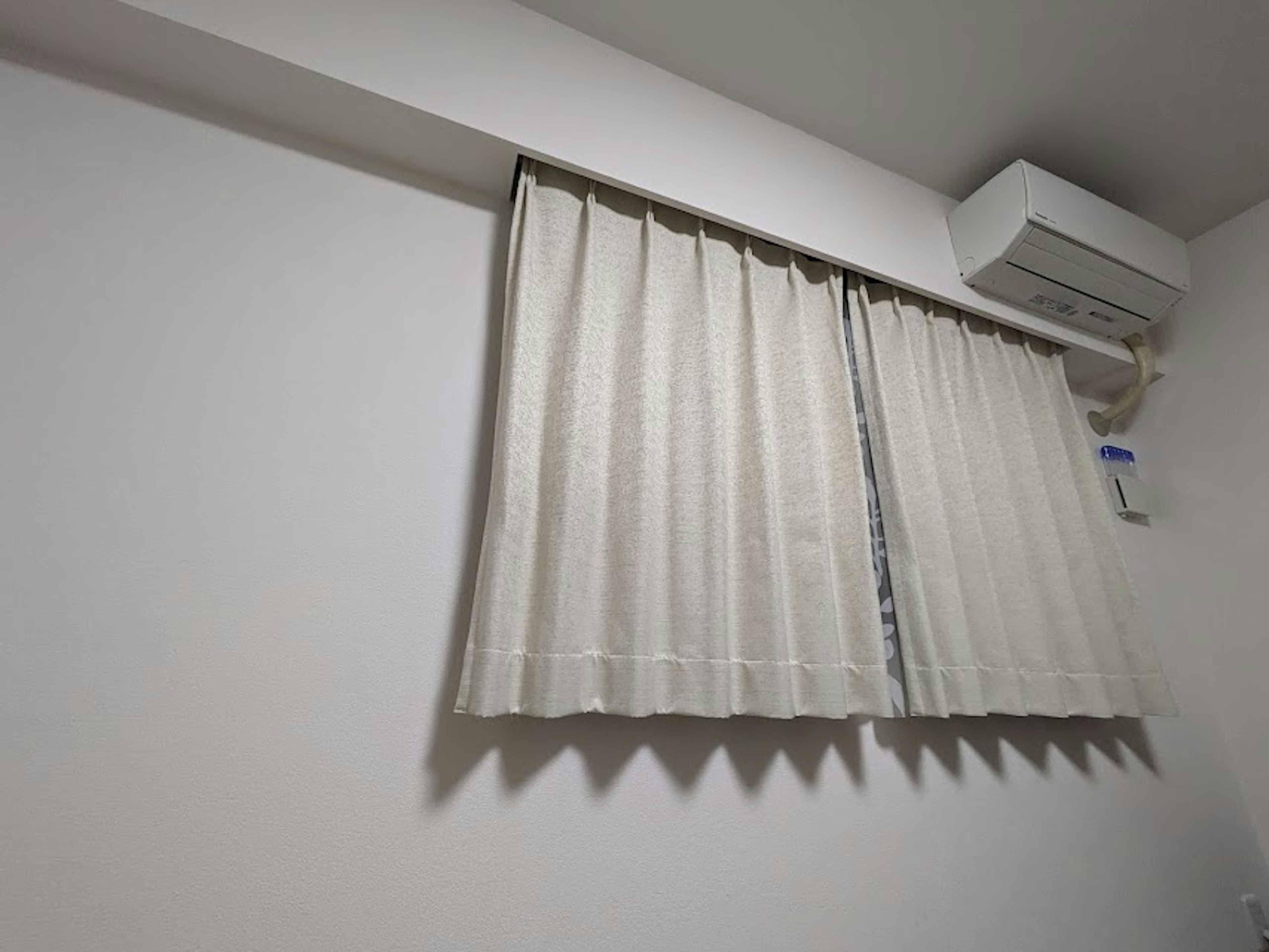 Parte de una habitación con una pared blanca, cortinas y un aire acondicionado