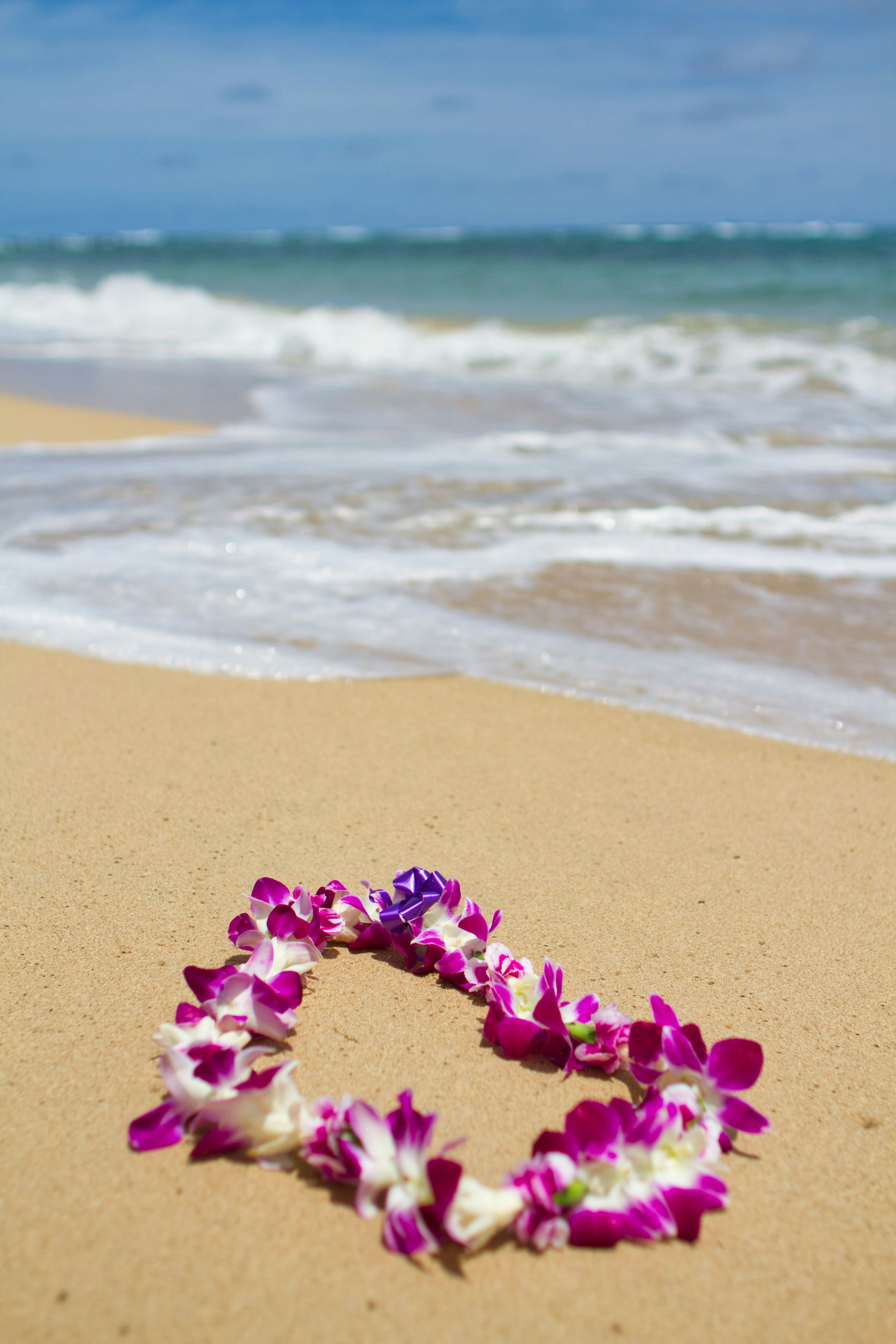 พวงมาลัยดอกไม้สีม่วงวางอยู่บนชายหาดทรายพร้อมคลื่นทะเล