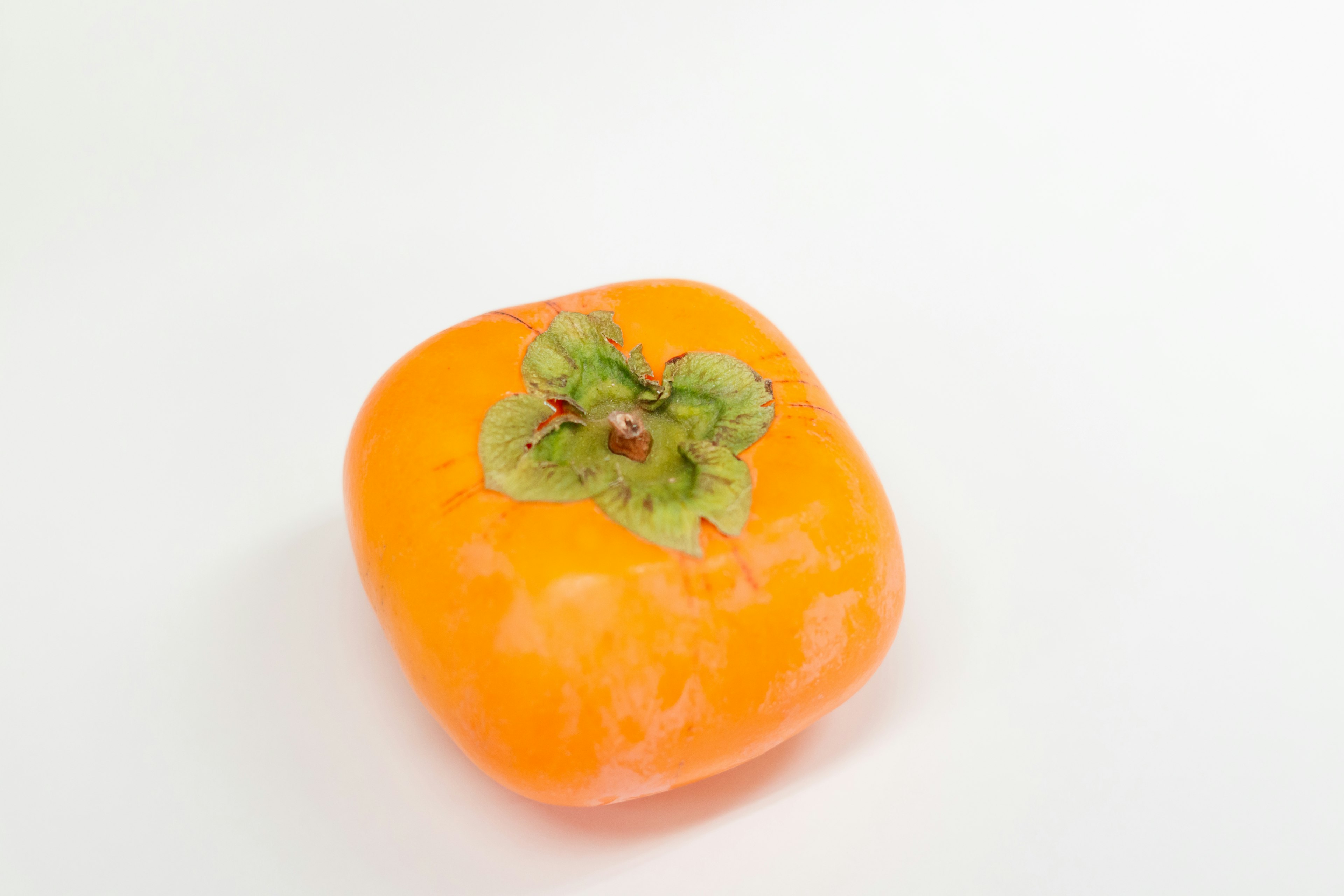 Un caqui naranja con una hoja verde sobre un fondo blanco