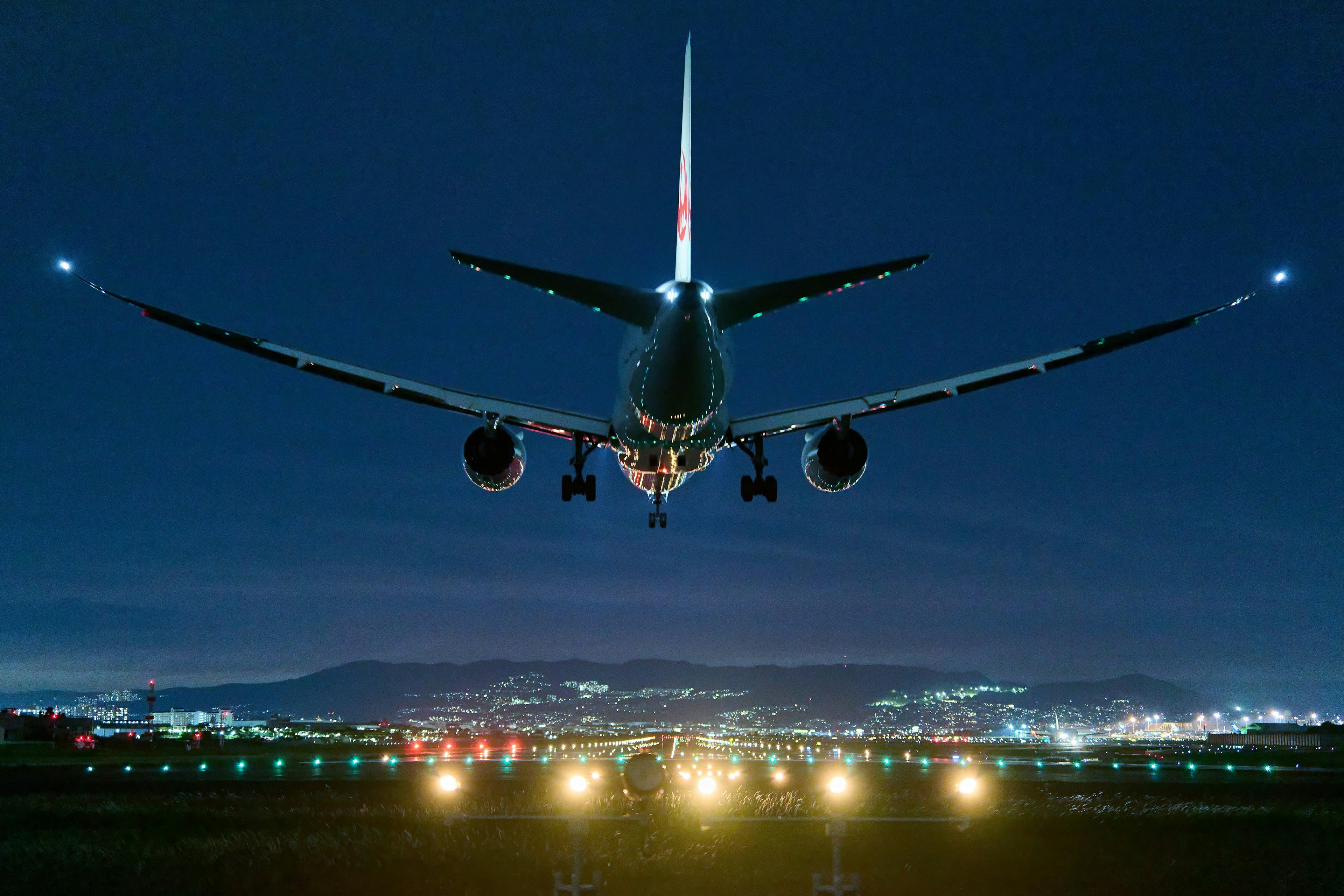 Un aereo che atterra su una pista di notte con luci della città sullo sfondo