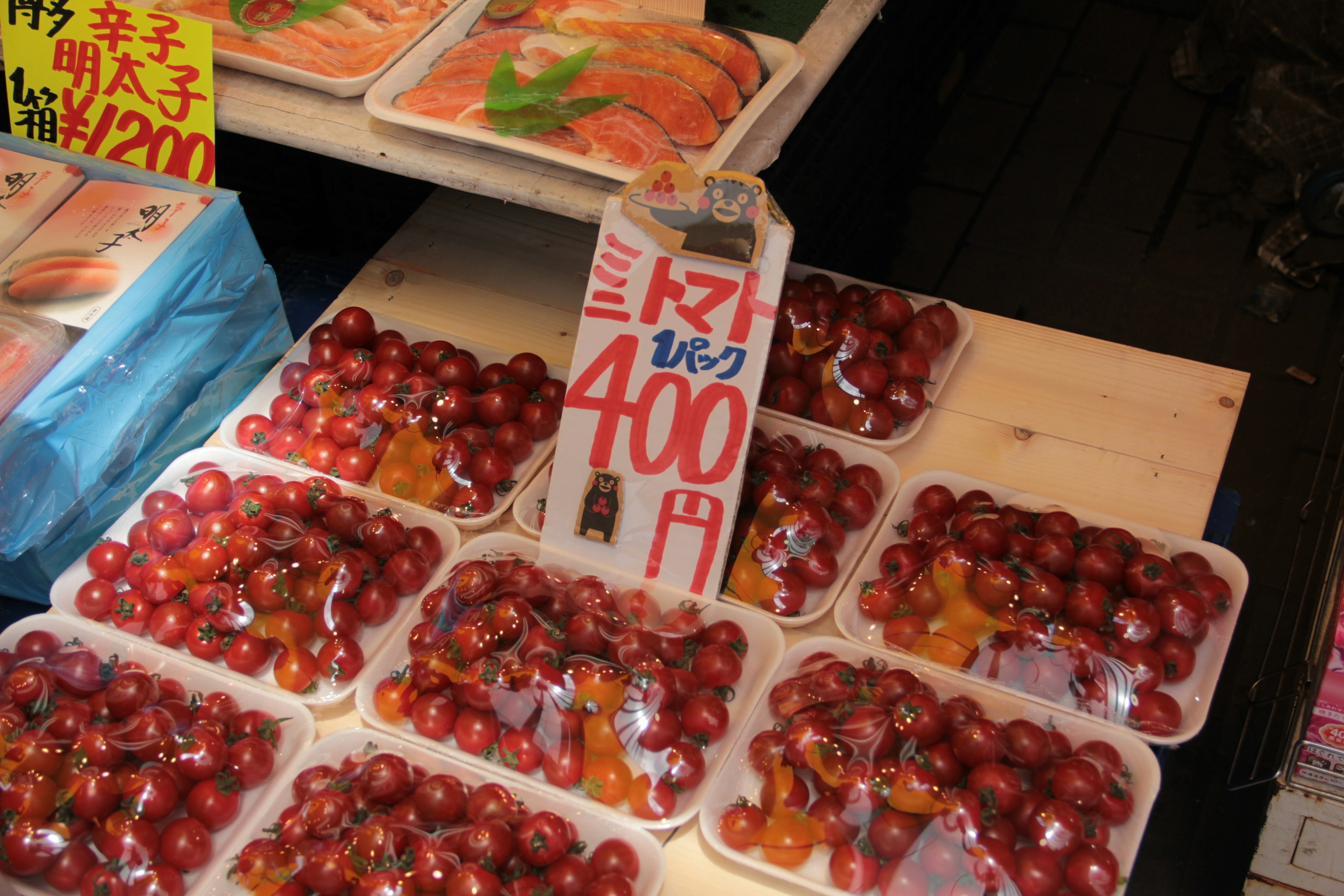 Exhibición de tomates cherry empaquetados en un mercado con cartel de precio