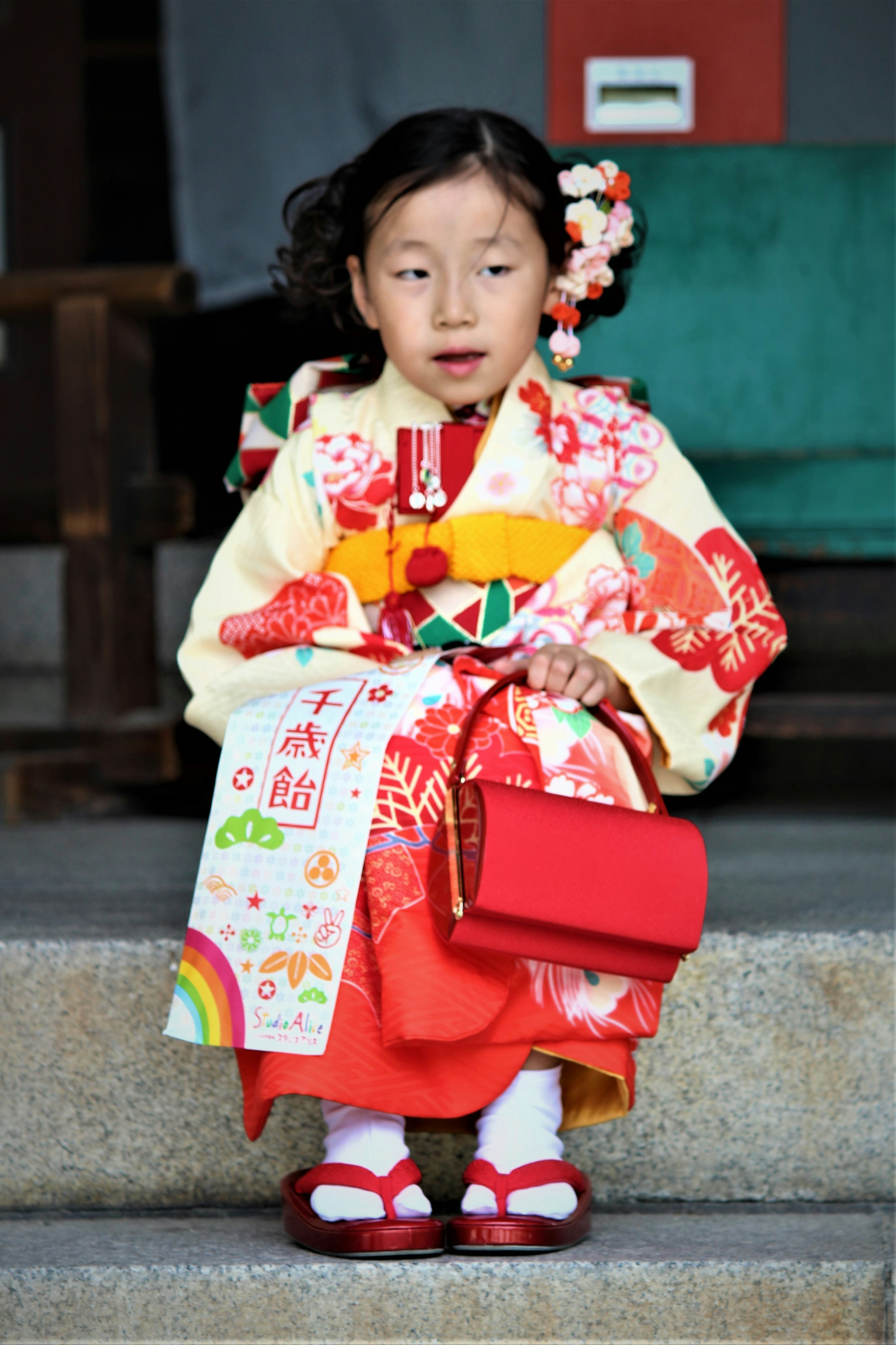 Anak mengenakan kimono tradisional sambil memegang tas merah