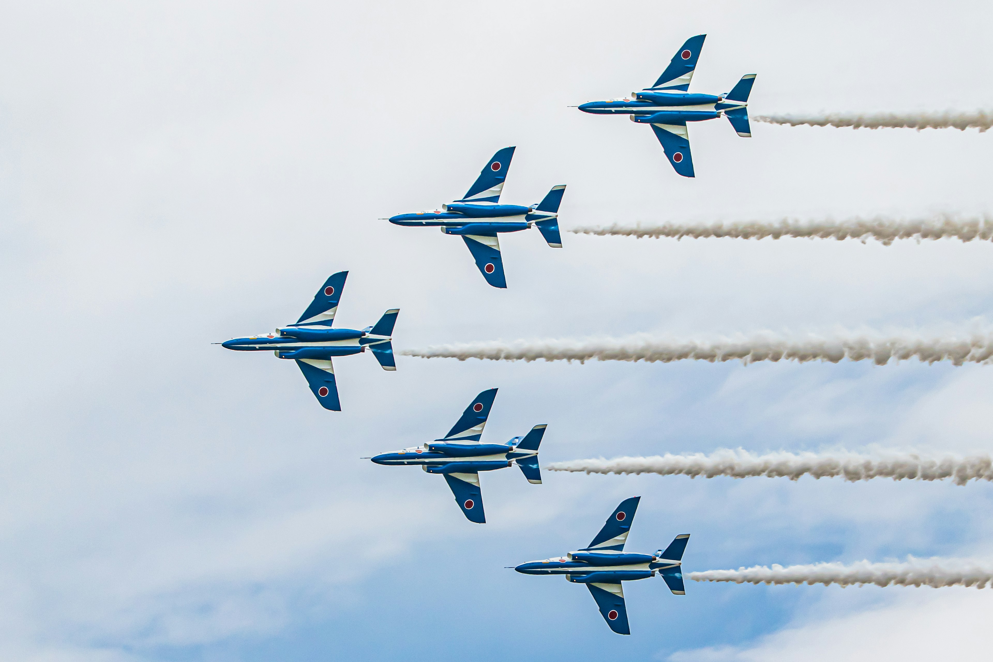 Blaue Jets fliegen in Formation mit weißen Rauchspuren