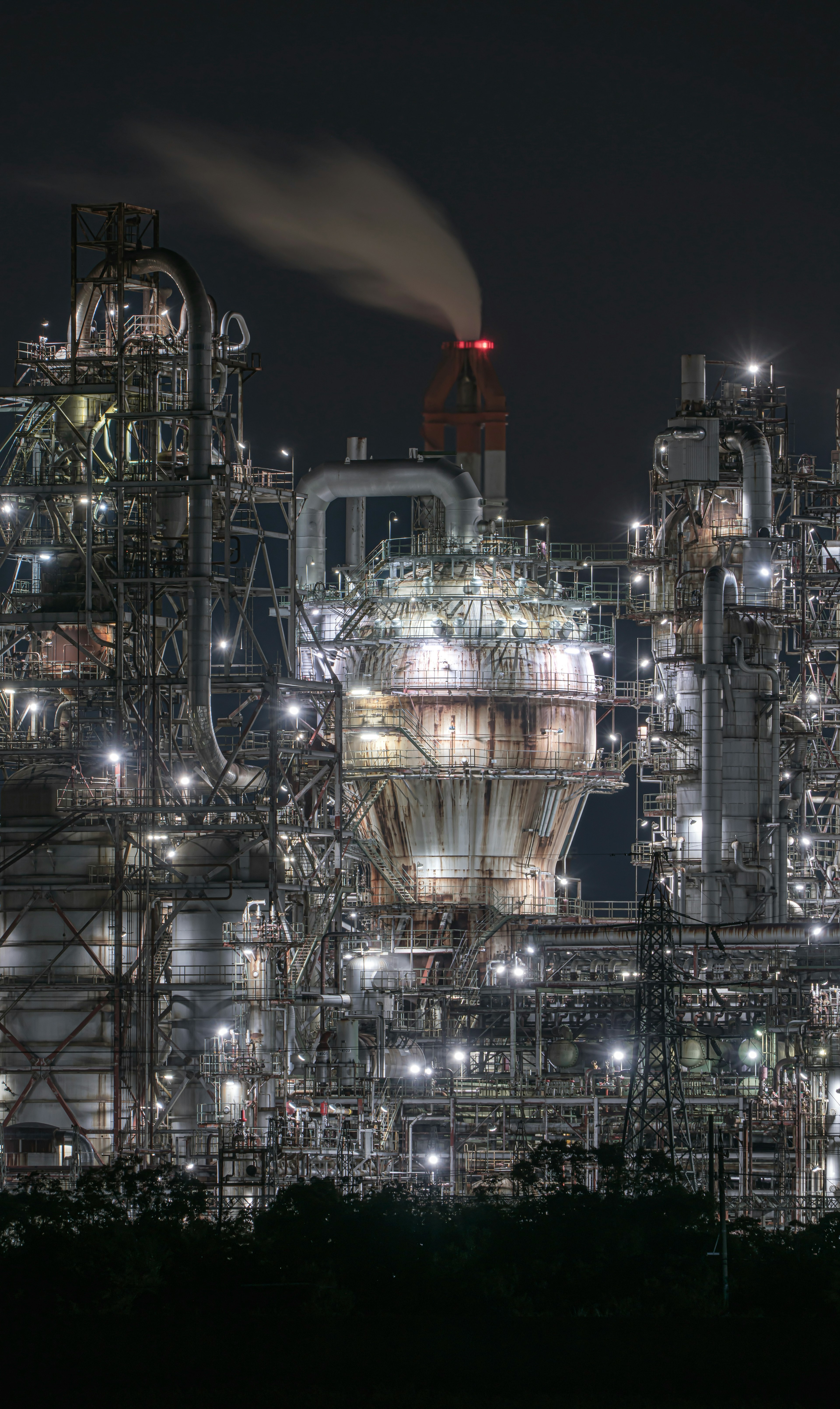 Bright industrial landscape at night featuring complex pipes and smokestacks